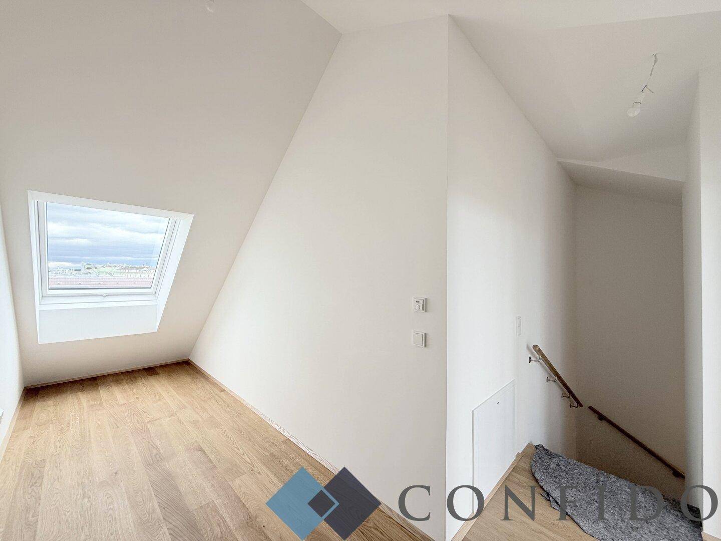 Dachgeschosszimmer mit schräger Decke, Dachfenster und Holzfußboden, bietet viel Tageslicht.