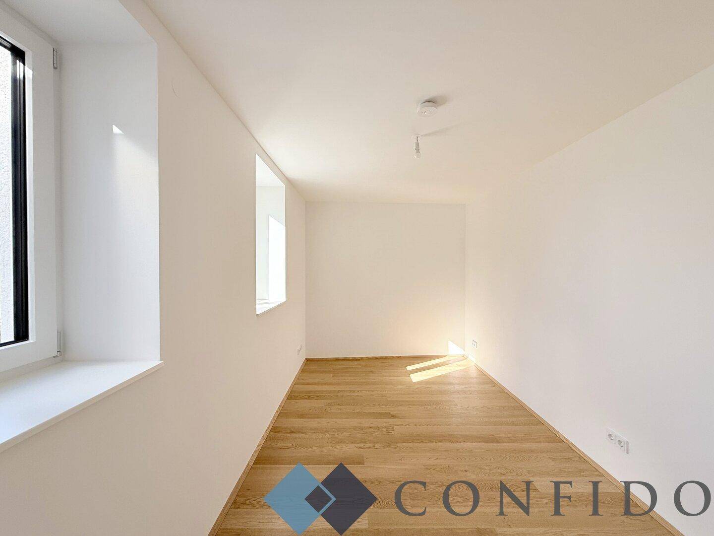 Helles Zimmer mit Holzboden und zwei Fenstern, ideal als Schlafzimmer oder Arbeitsbereich.