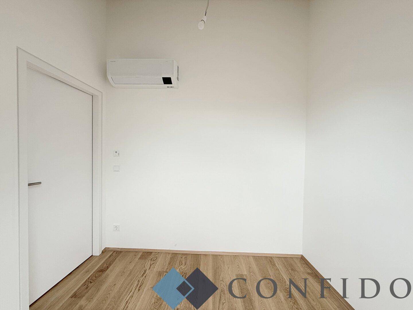 Leeres Zimmer mit Parkettboden und Klimaanlage, bietet flexible Nutzungsmöglichkeiten.