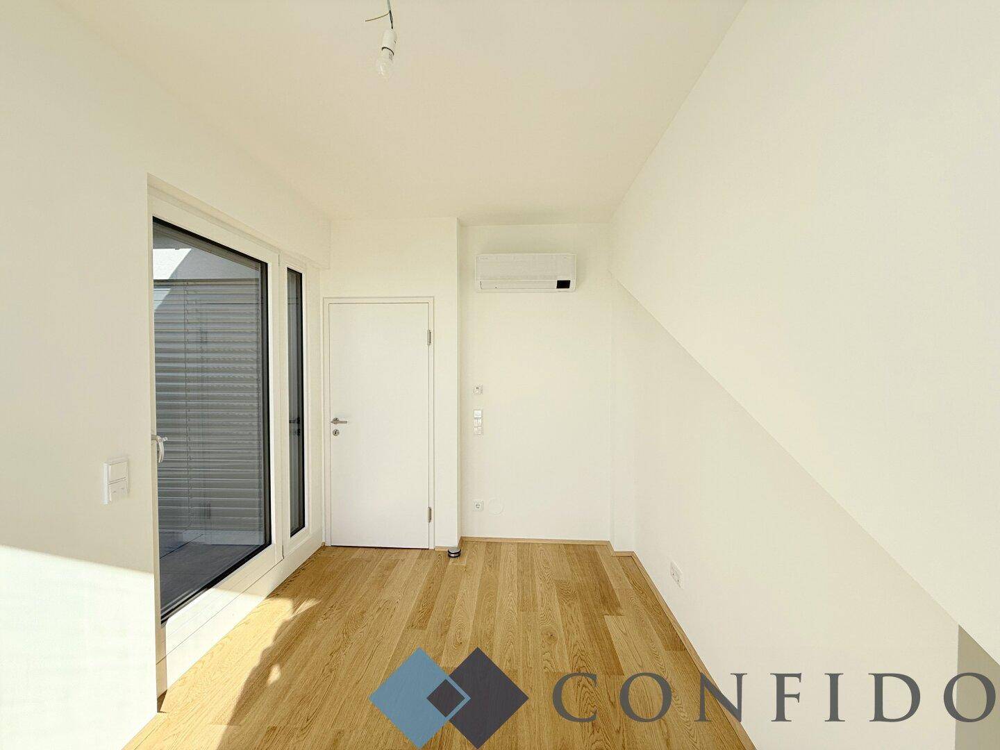 Dachgeschosszimmer mit schräger Decke, Klimaanlage und Zugang zu einer kleinen Terrasse.