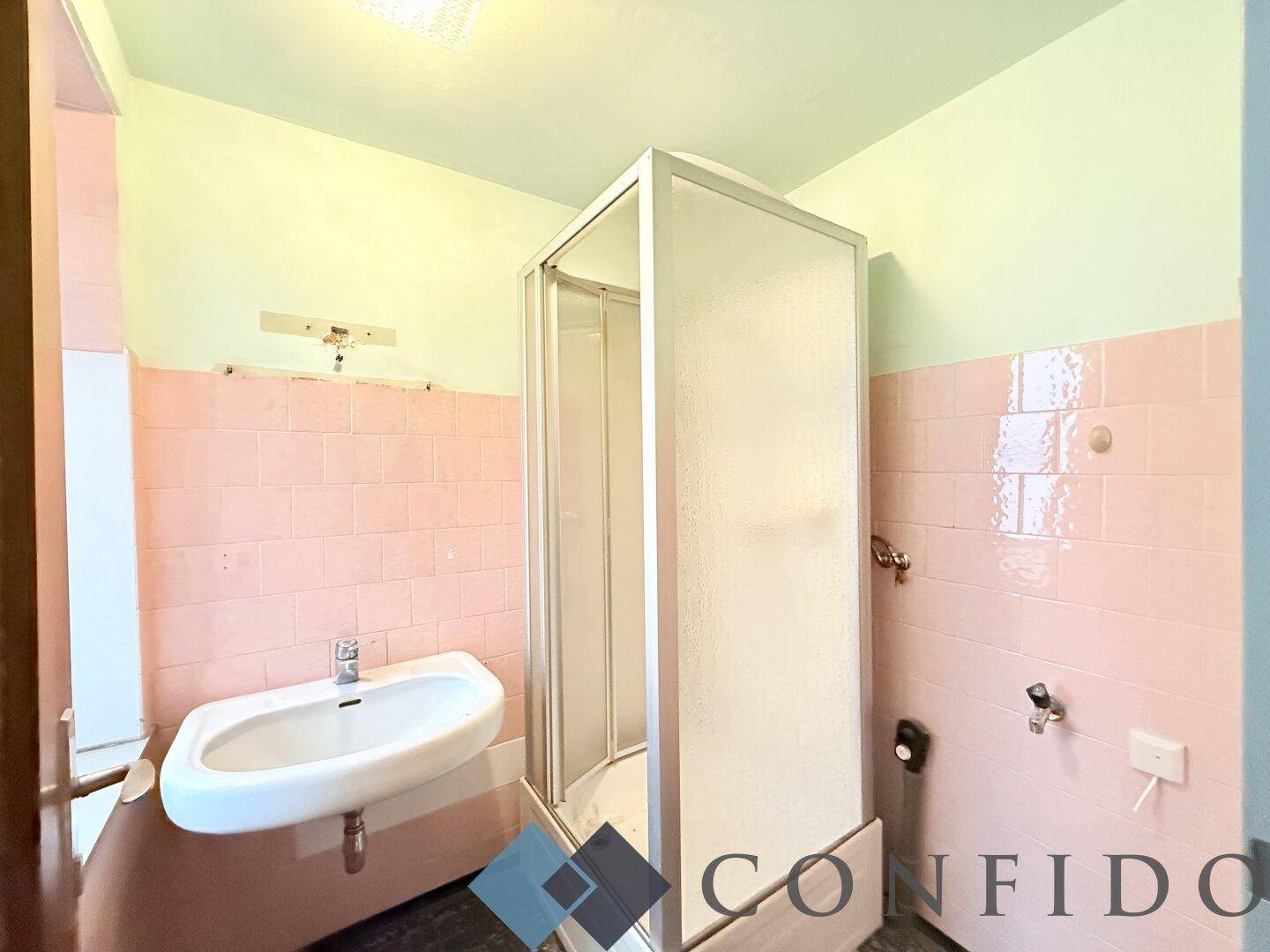 Badezimmer mit rosa Fliesen, Waschbecken und Duschkabine, das eine Modernisierung benötigt.
