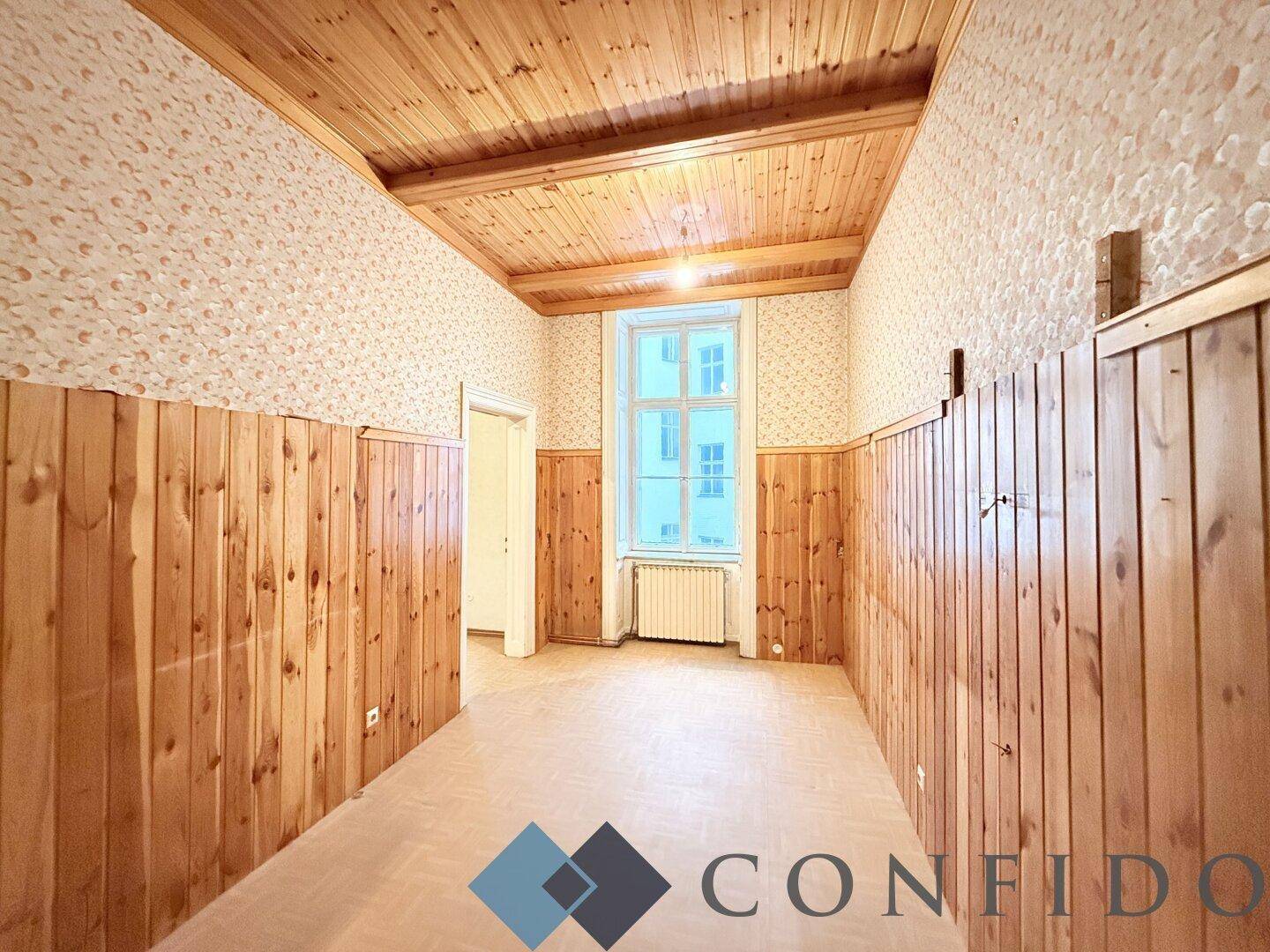 Zimmer mit Holzvertäfelung an Wänden und Decke sowie einem großen Fenster.