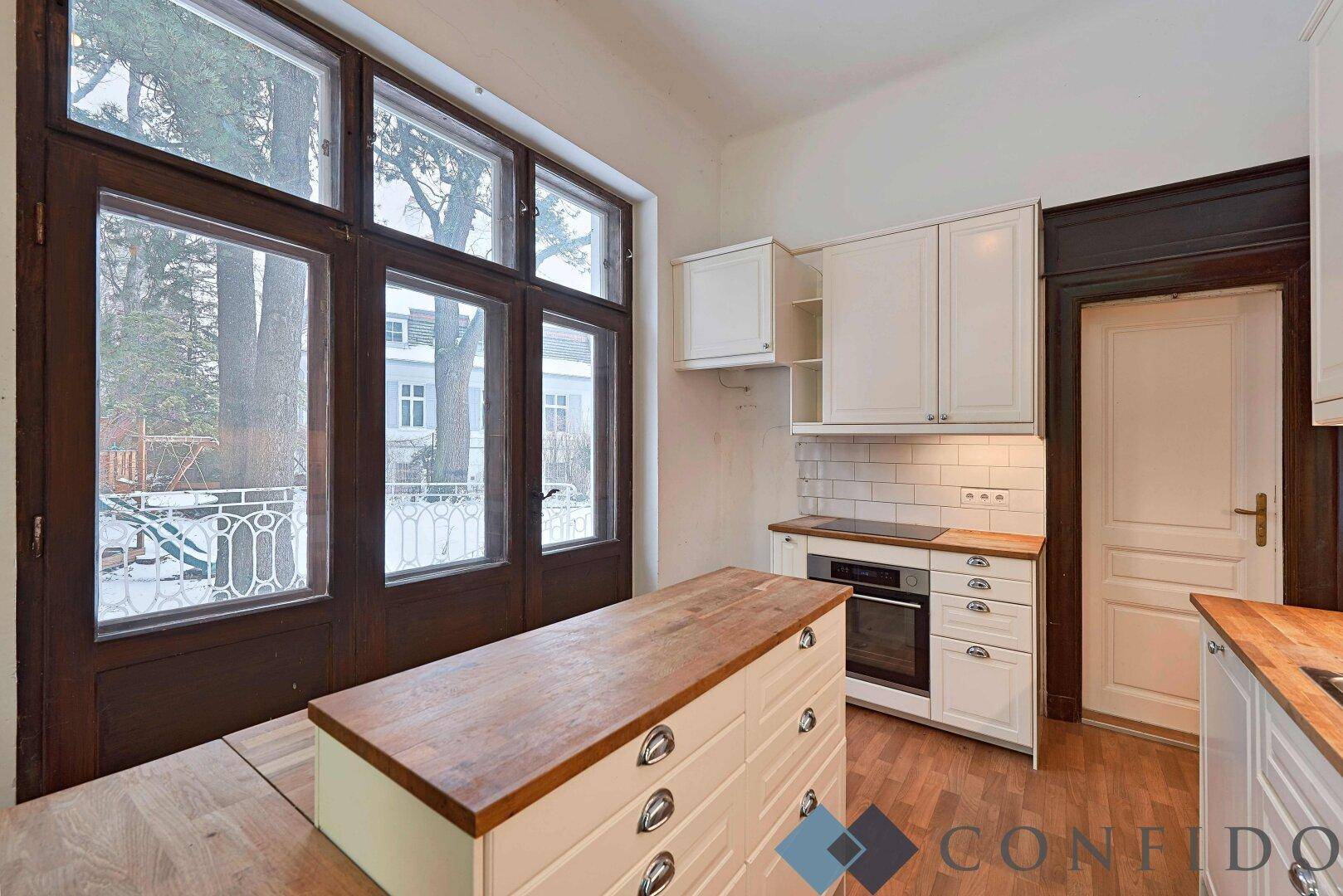 Helle Küche mit Holzarbeitsplatten, weißen Schränken und Zugang zum Balkon.