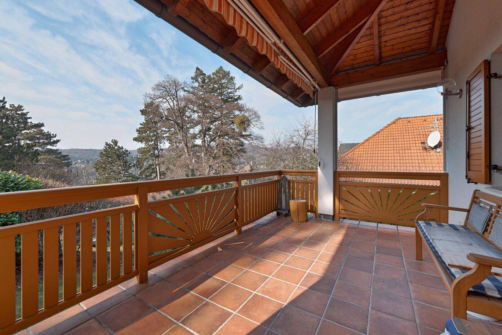 Überdachter Balkon mit Terrakottafliesen, Holzgeländer und Sitzgelegenheiten mit Weitblick.