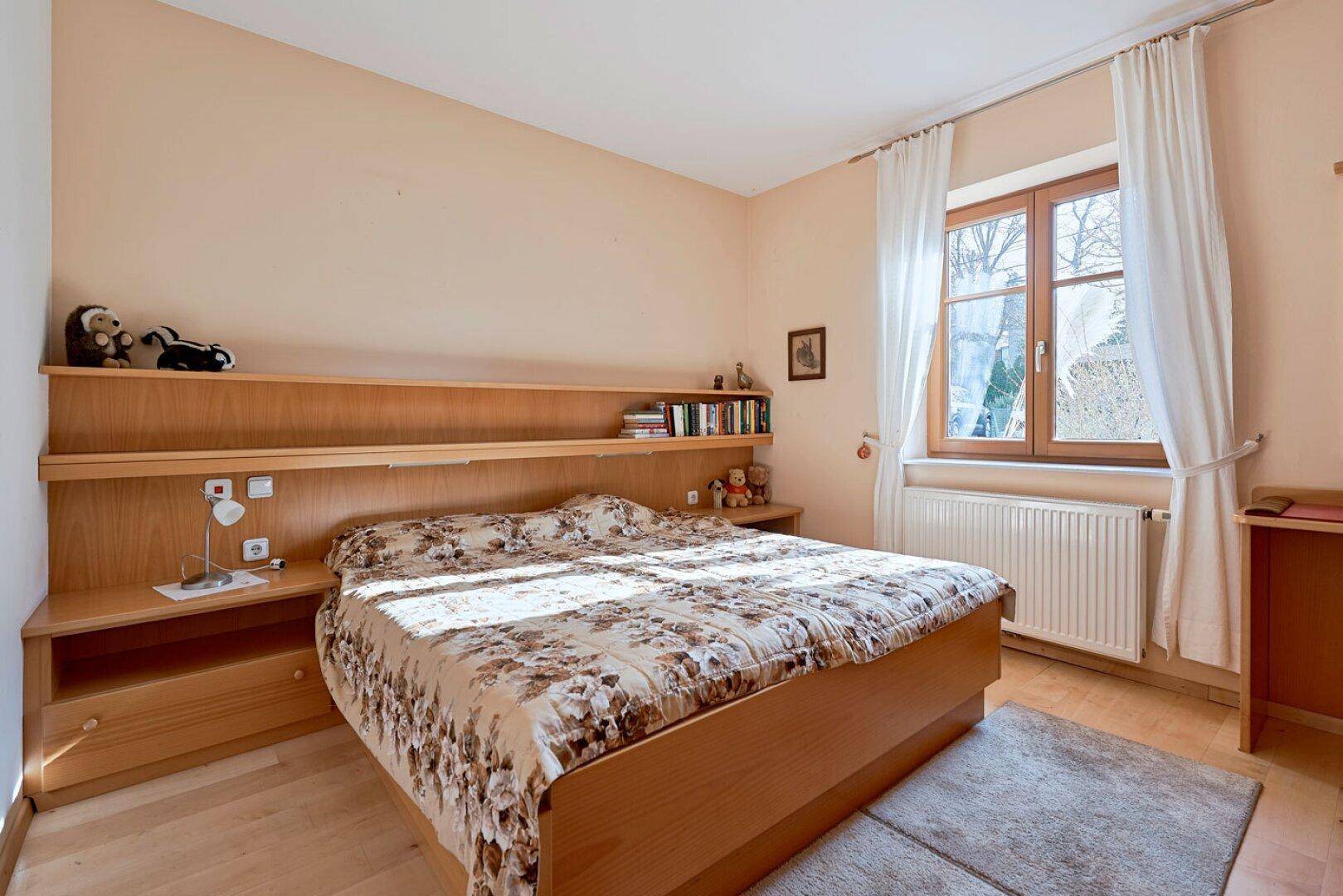 Helles Schlafzimmer mit Holzboden, großem Bett und integrierten Nachttischen unter einem Fenster.