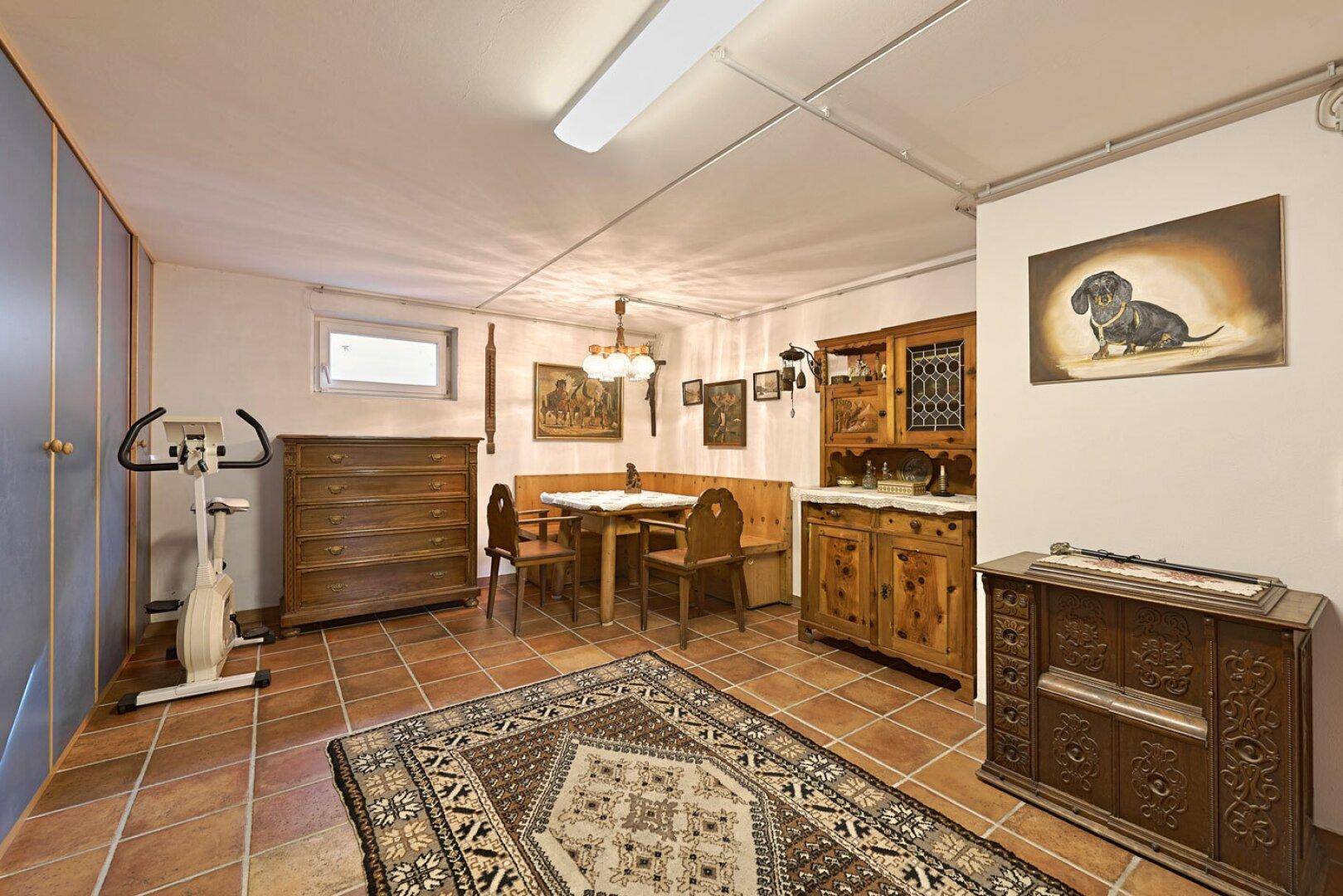 Ausgebauter Kellerraum mit traditionellen Holzmöbeln, Essbereich und einem Heimtrainer.