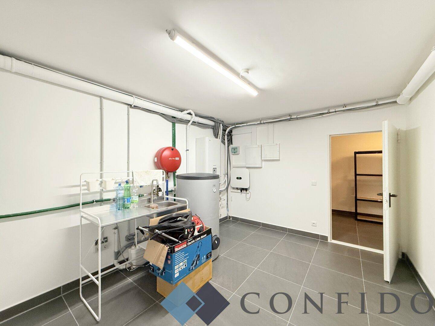 Funktionaler Hauswirtschaftsraum im Keller mit Waschbecken, Warmwasserbereiter und Installationen.