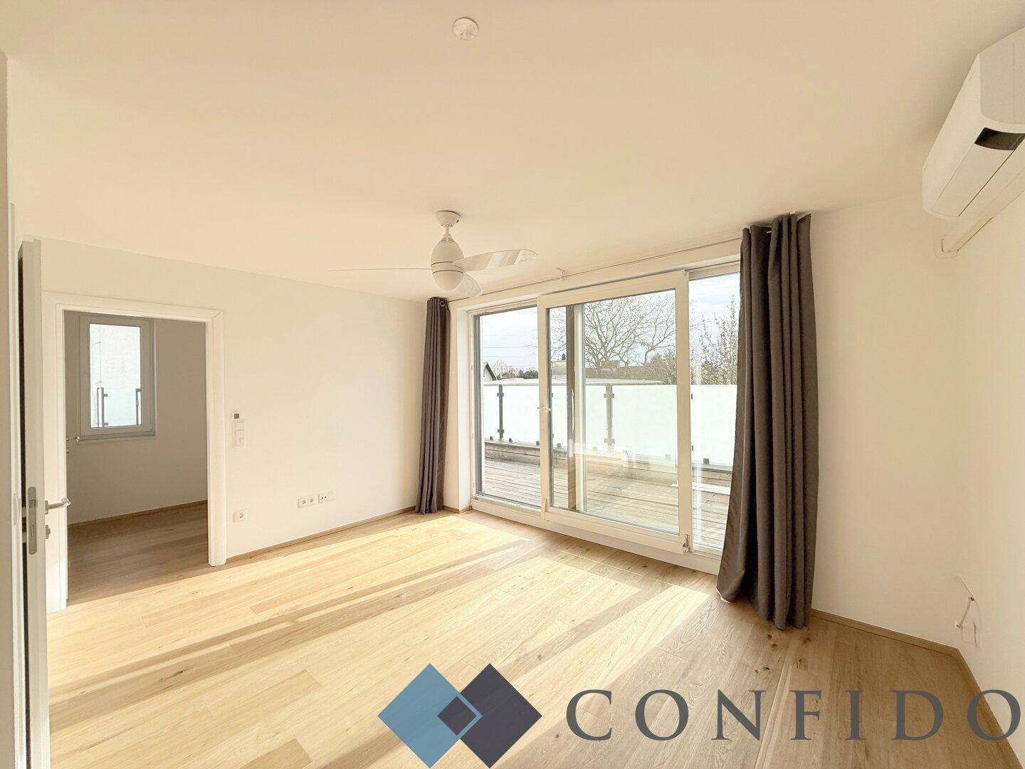 Helles Zimmer mit Holzboden, Deckenventilator und Zugang zu einem Balkon oder einer Terrasse.