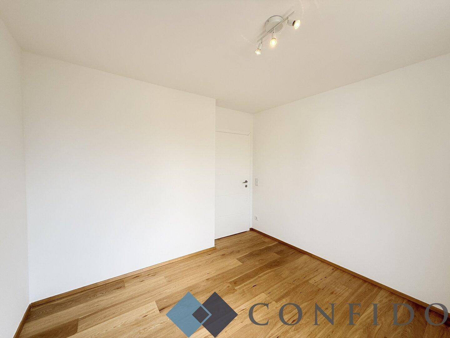 Einfaches Schlafzimmer mit Holzboden und weiß gestrichenen Wänden, bereit zur individuellen Gestaltung.