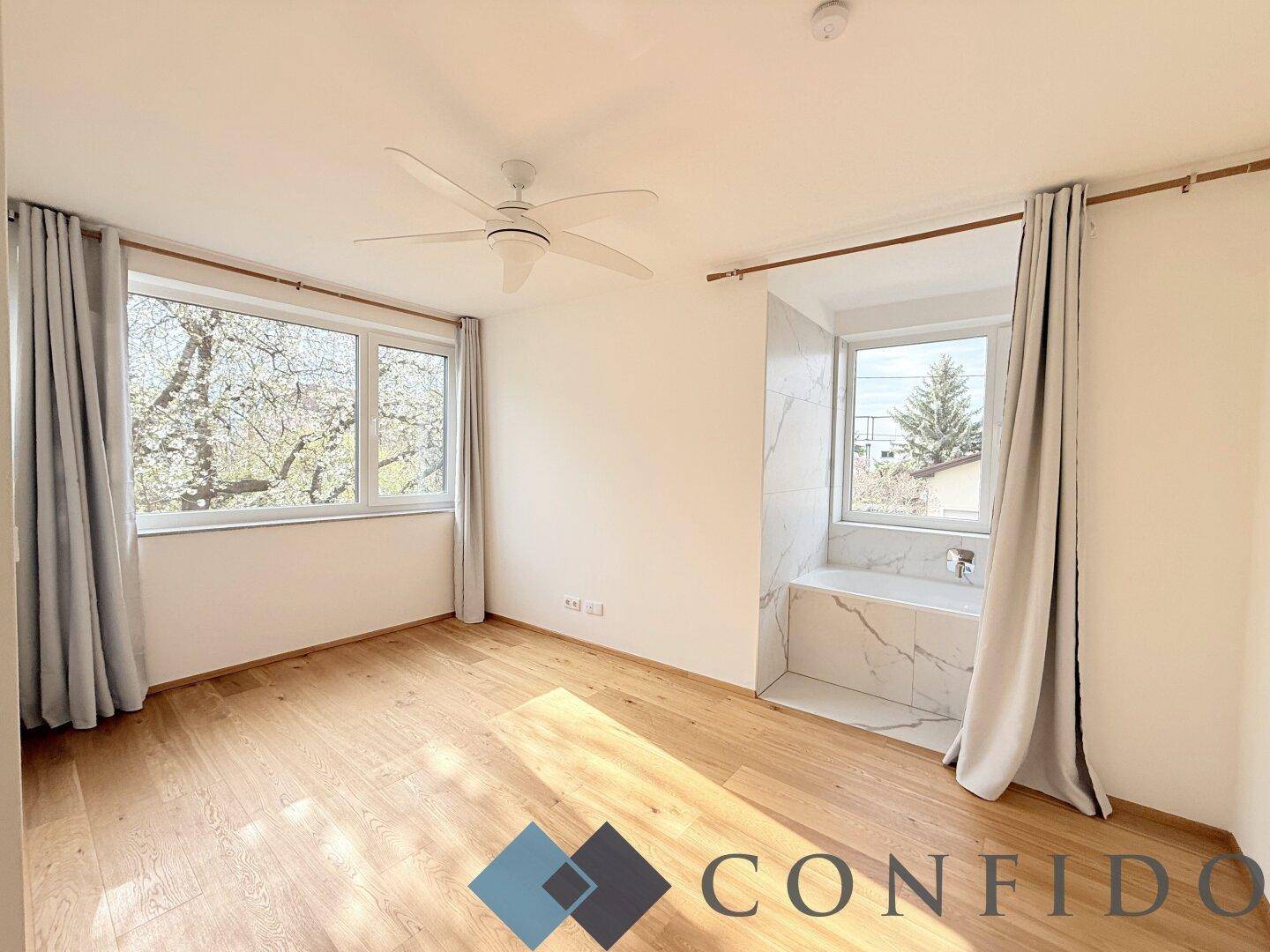 Helles Schlafzimmer mit Holzboden, Deckenventilator und integriertem Badewannenbereich.