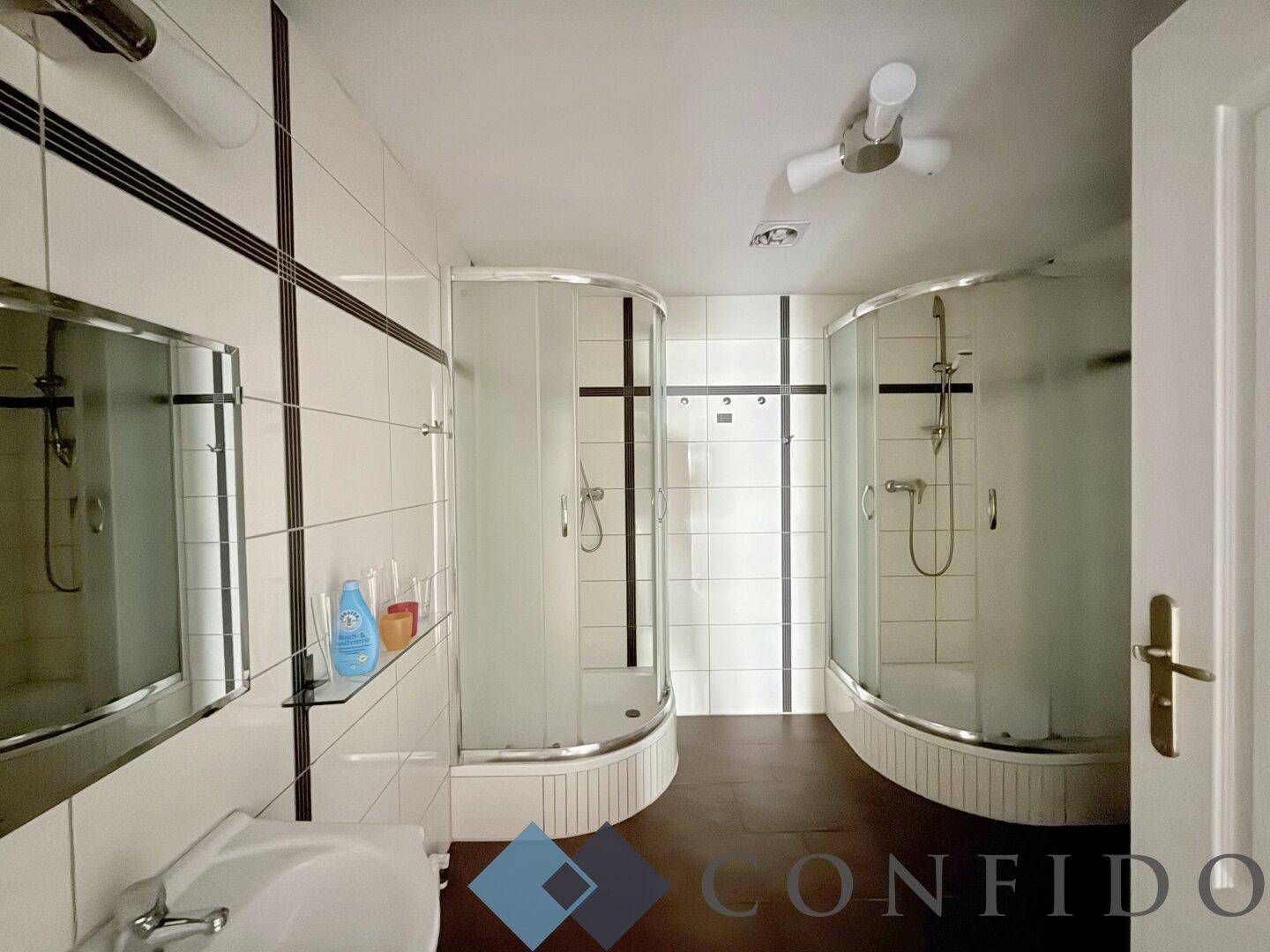 Badezimmer mit zwei Duschkabinen, Waschbecken und Fliesen an Wänden und Boden.