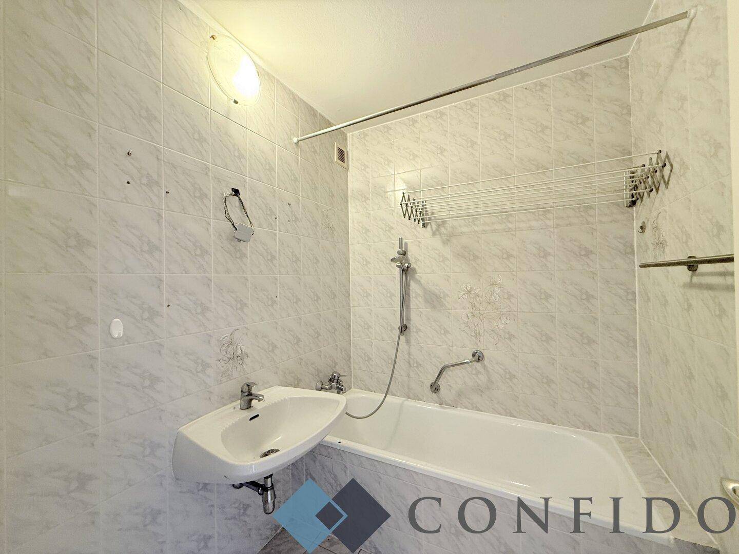 Badezimmer mit Badewanne, Waschbecken und hellen Wandfliesen im 80er-Jahre-Stil.