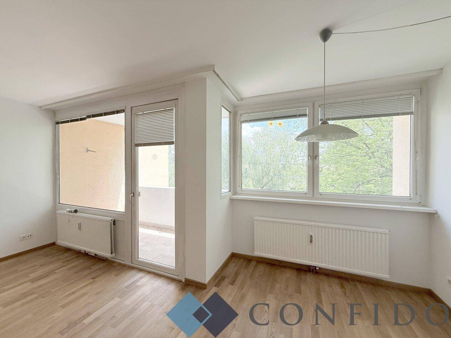 Helles Wohnzimmer mit großen Fenstern, Blick ins Grüne und Zugang zum Balkon.