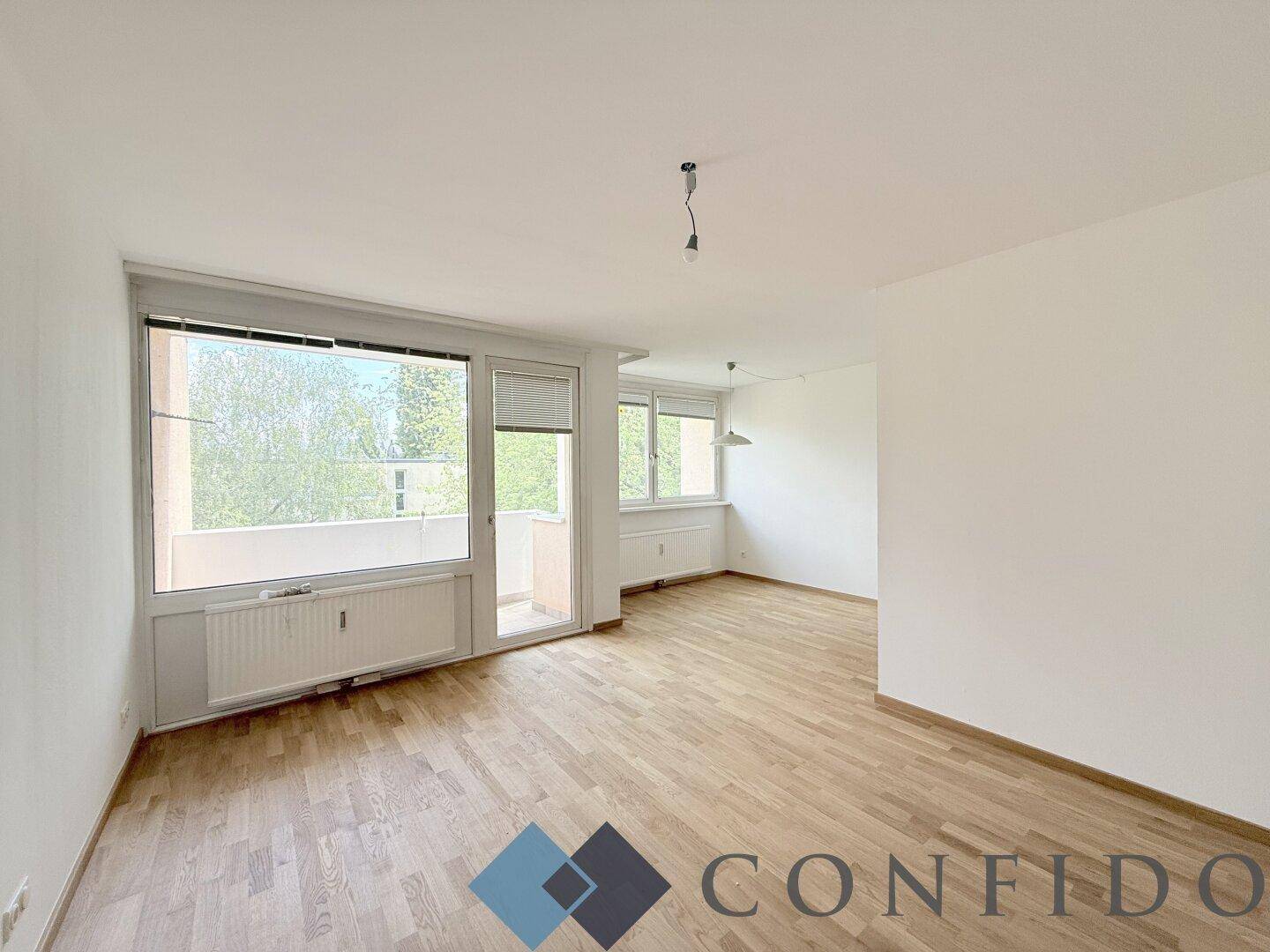 Geräumiges Wohnzimmer mit Parkettboden, großen Fenstern und Zugang zum Balkon.