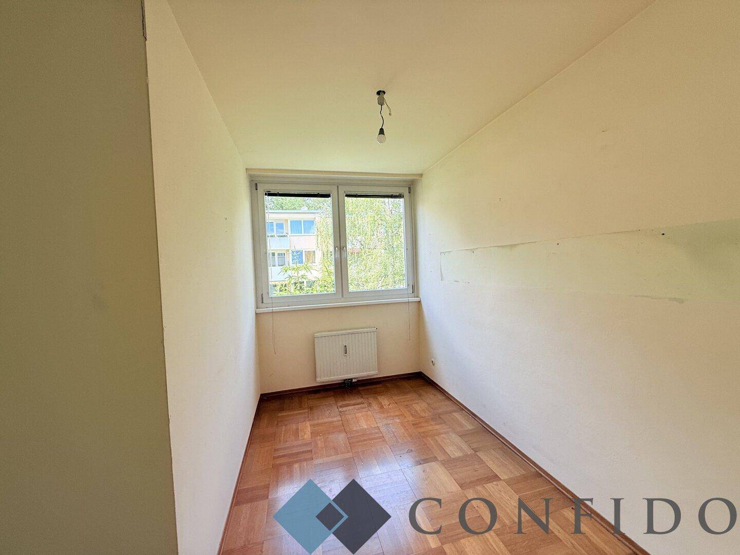 Helles Schlafzimmer mit Parkettboden und Fenster, bereit zur individuellen Gestaltung.