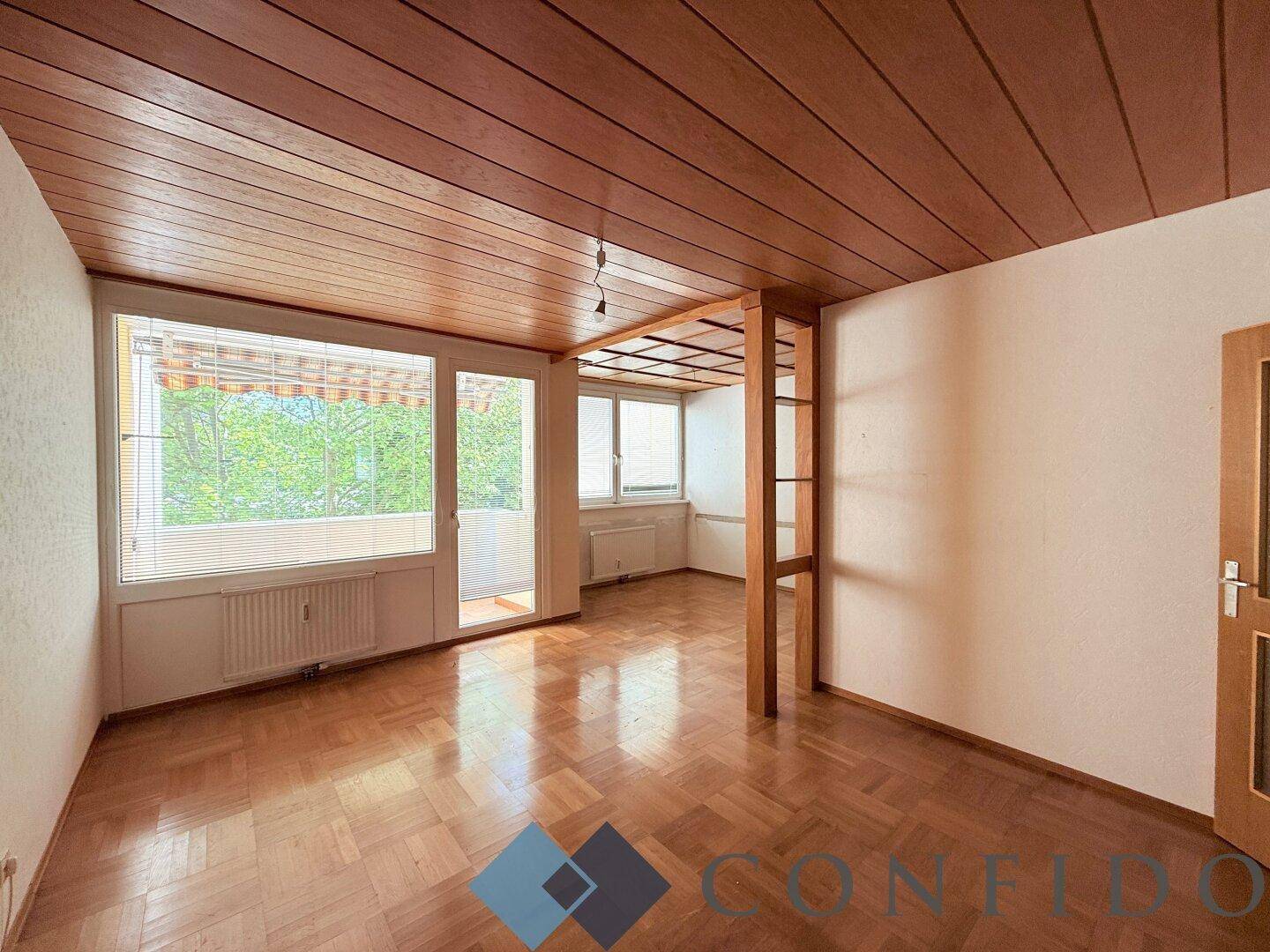Geräumiges Wohnzimmer mit Parkettboden, Holzdecke und Zugang zum Balkon.