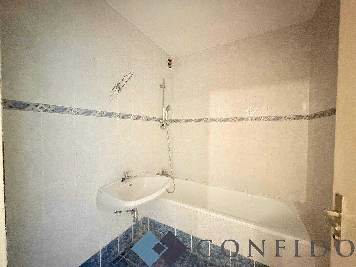 Badezimmer mit blauen und weißen Fliesen, ausgestattet mit Badewanne und integrierter Dusche sowie Waschbecken.