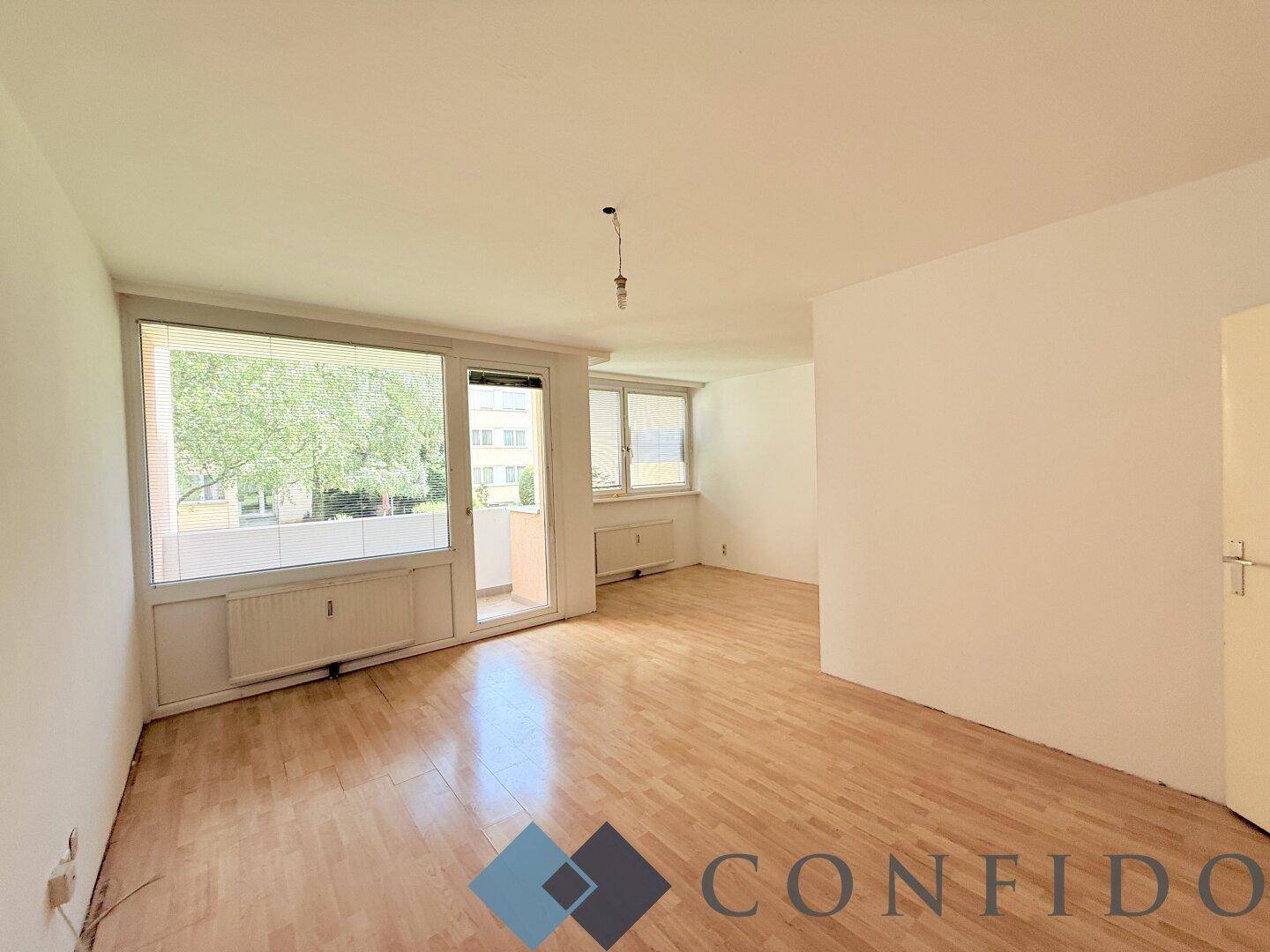 Helles Wohnzimmer mit Parkettboden und Zugang zu einem Balkon, bietet viel Tageslicht.