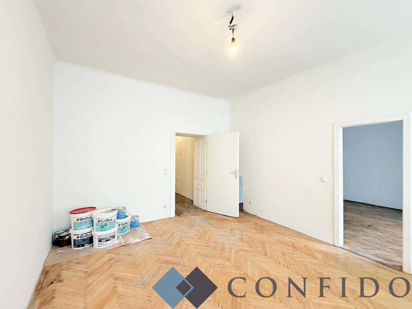 Geräumiges Zimmer mit Fischgrätparkett und Farbeimern, bereit für die Renovierung.