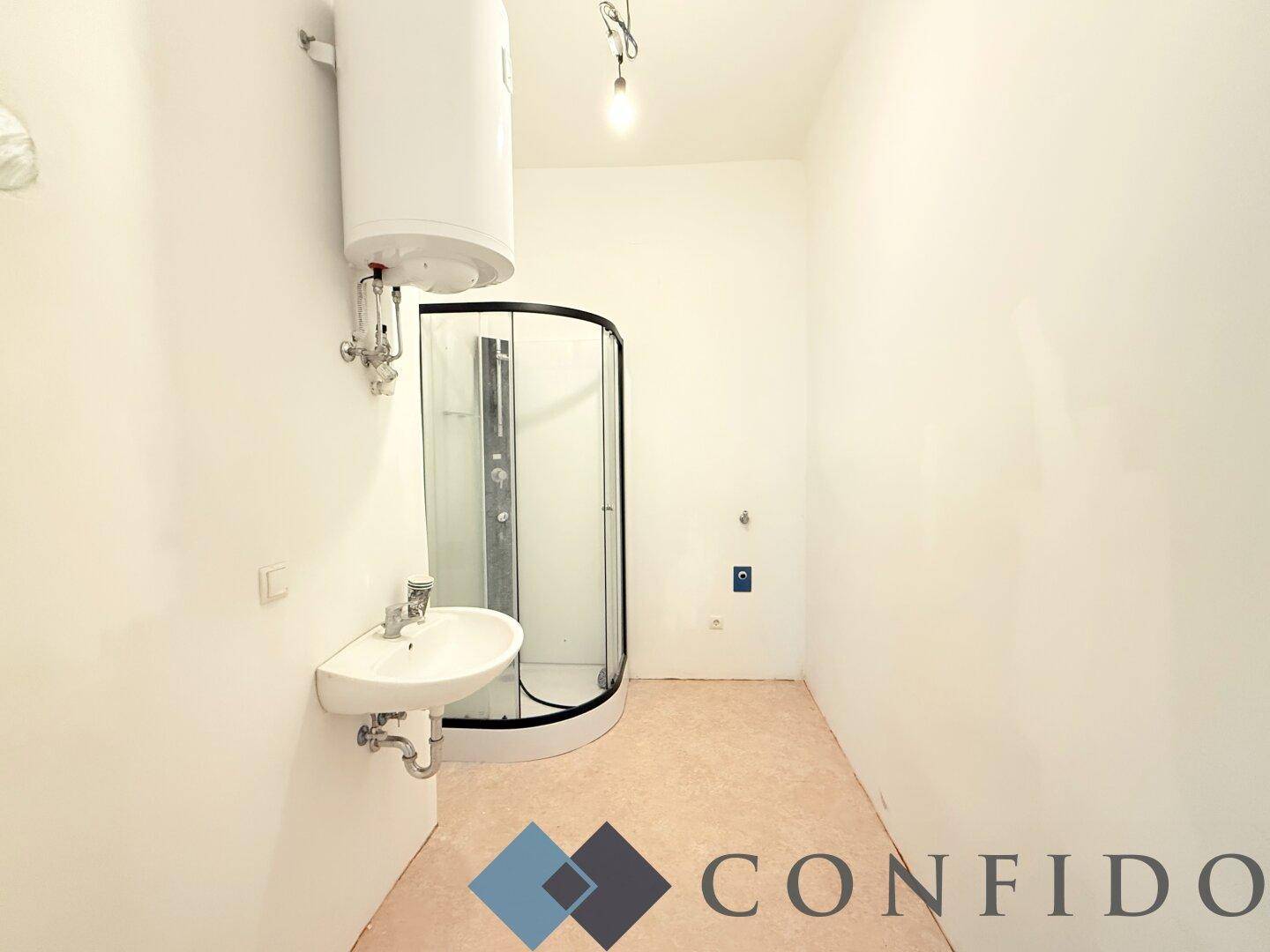 Einfaches Badezimmer mit Dusche, Waschbecken und Warmwasserboiler, funktional und hell.