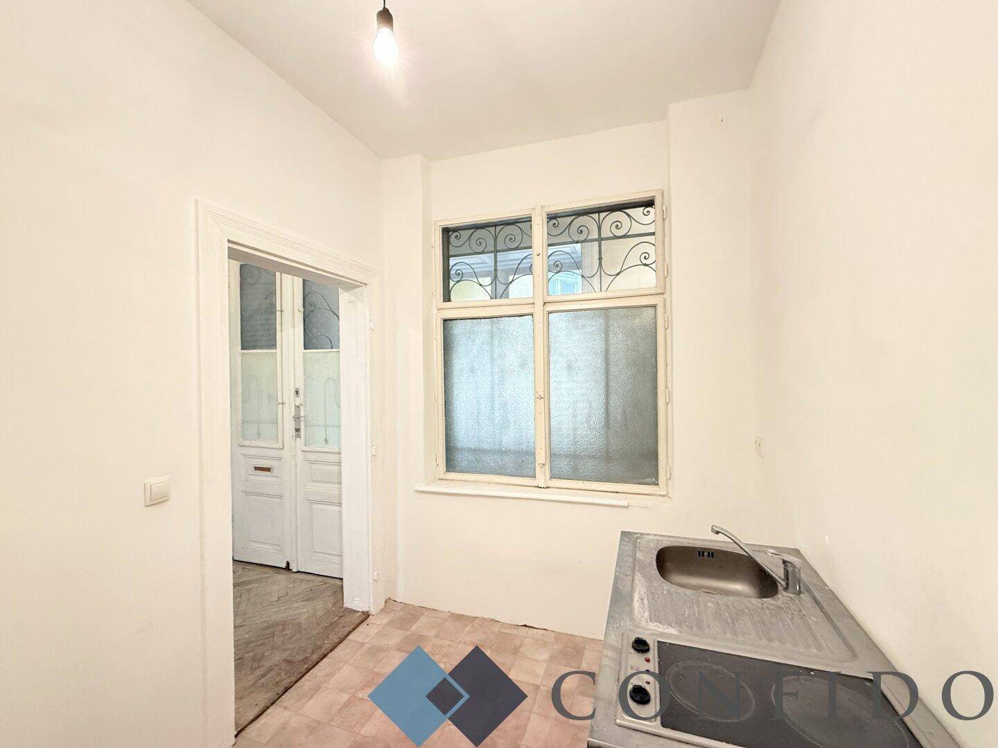 Kleine Küche mit Spüle, Kochfeld und Fenster mit schmiedeeisernem Gitter im Originalzustand.