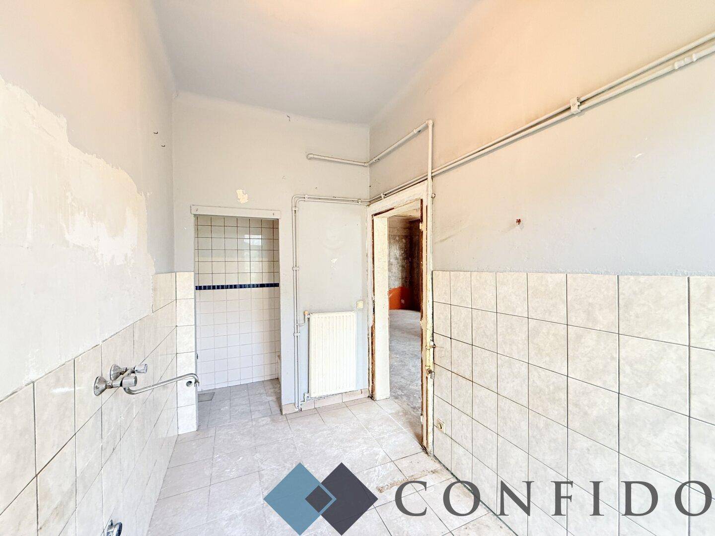 Gefliester Raum mit Heizkörper und mehreren Türöffnungen, bereit für die Badezimmerinstallation.