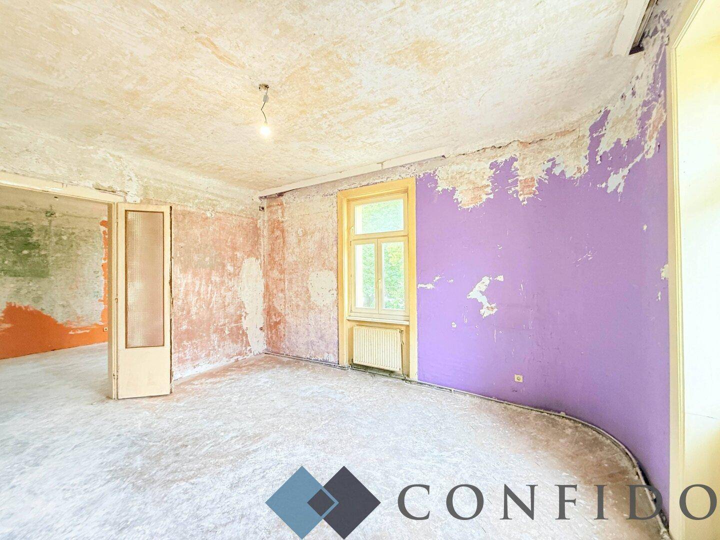 Weiterer Blick in den renovierungsbedürftigen Raum mit lila Wand und einer Türöffnung.