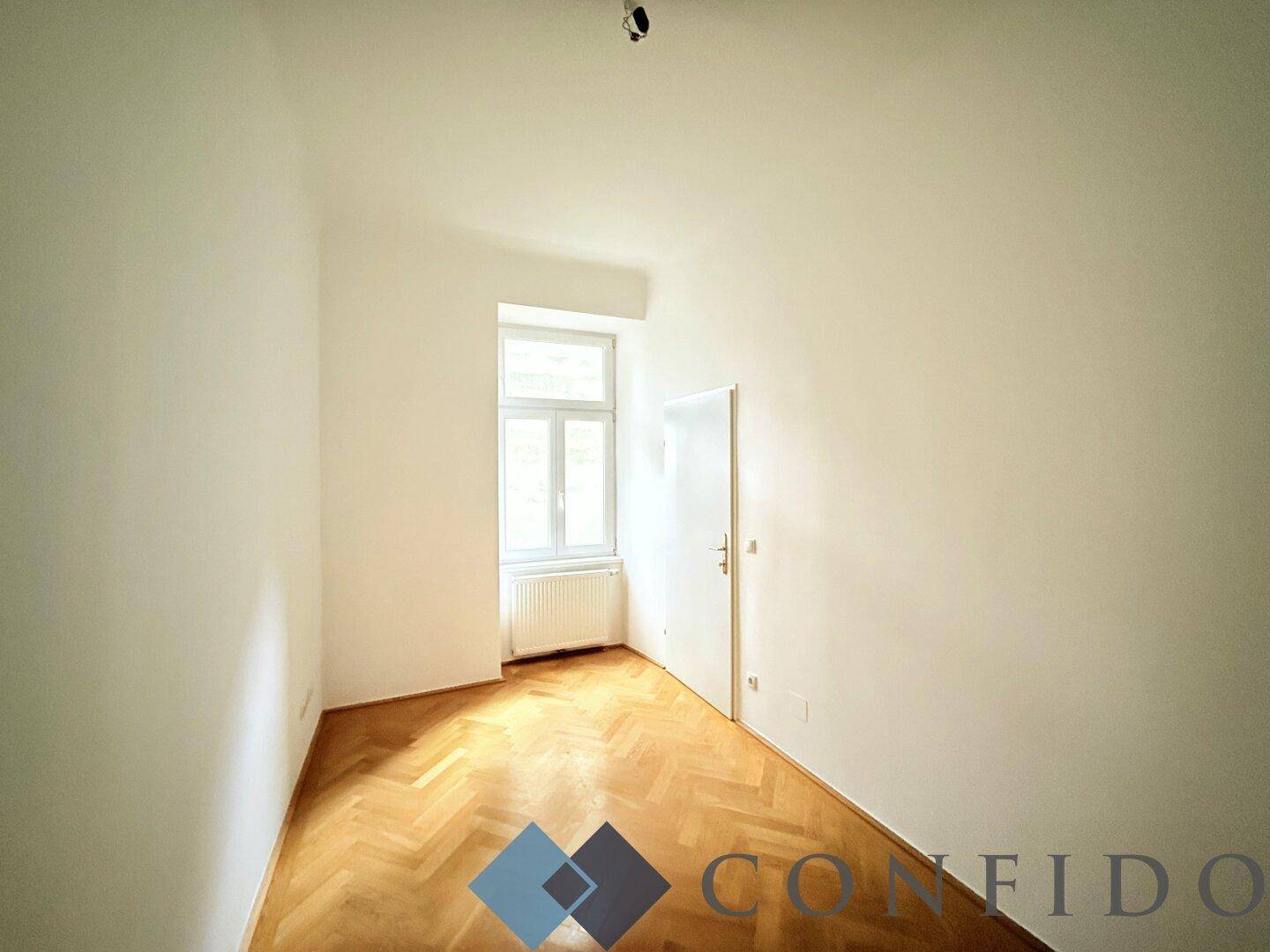 Gemütliches Zimmer mit Parkettboden, Fenster und weiß gestrichenen Wänden.