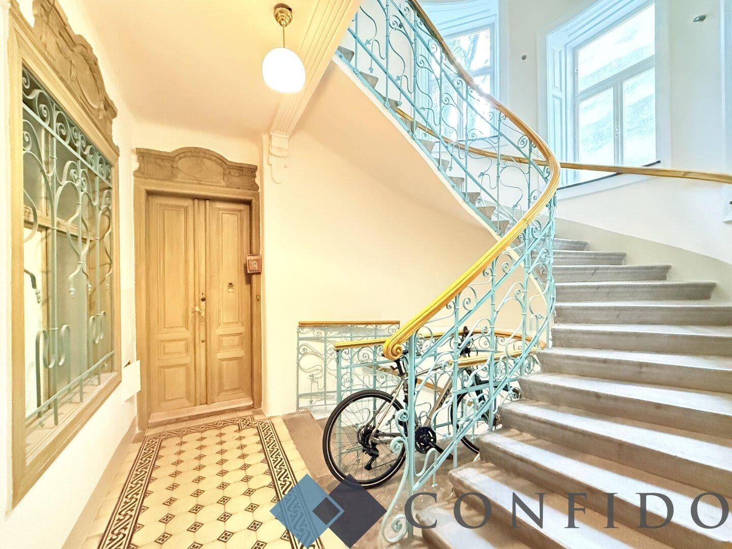 Prunkvolles Treppenhaus mit kunstvollen Geländern und historischen Fliesen, zeugt von Altbau-Eleganz.