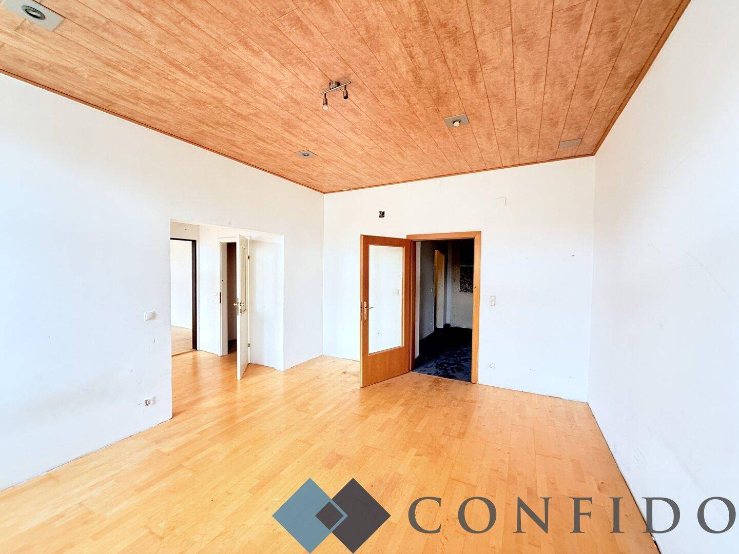 Geräumiges Zimmer mit Parkettboden und Holzdecke, bietet Zugang zu weiteren Räumen.