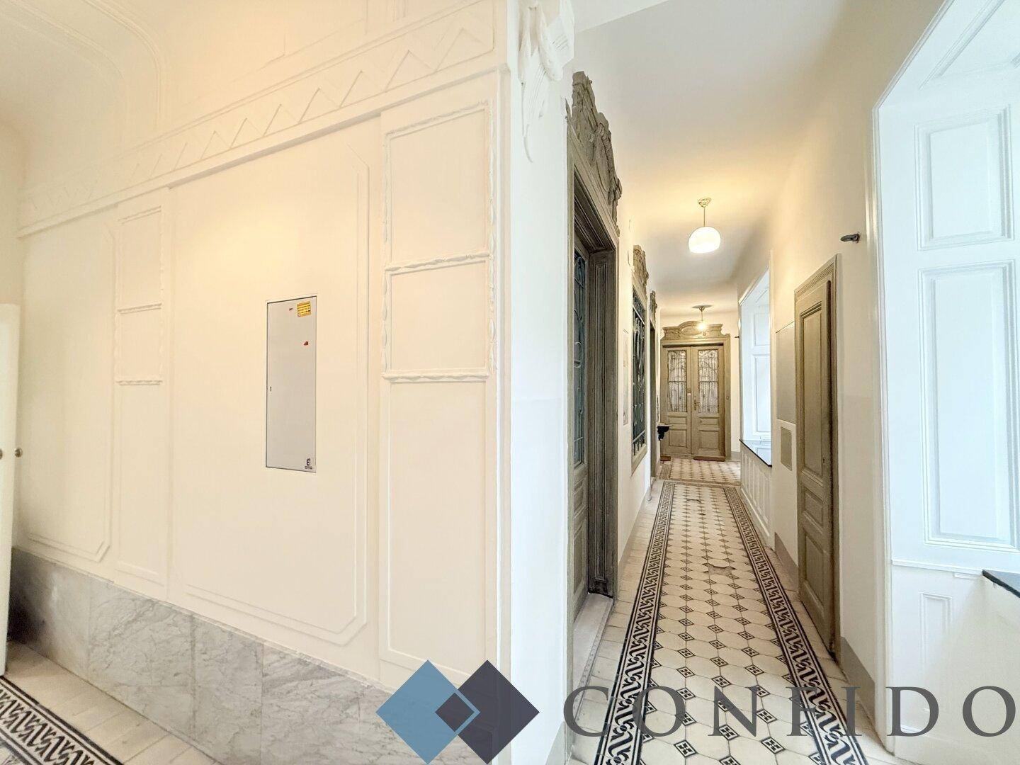 Langer Flur im Altbau mit gemustertem Fliesenboden und dekorativen Wandpaneelen.