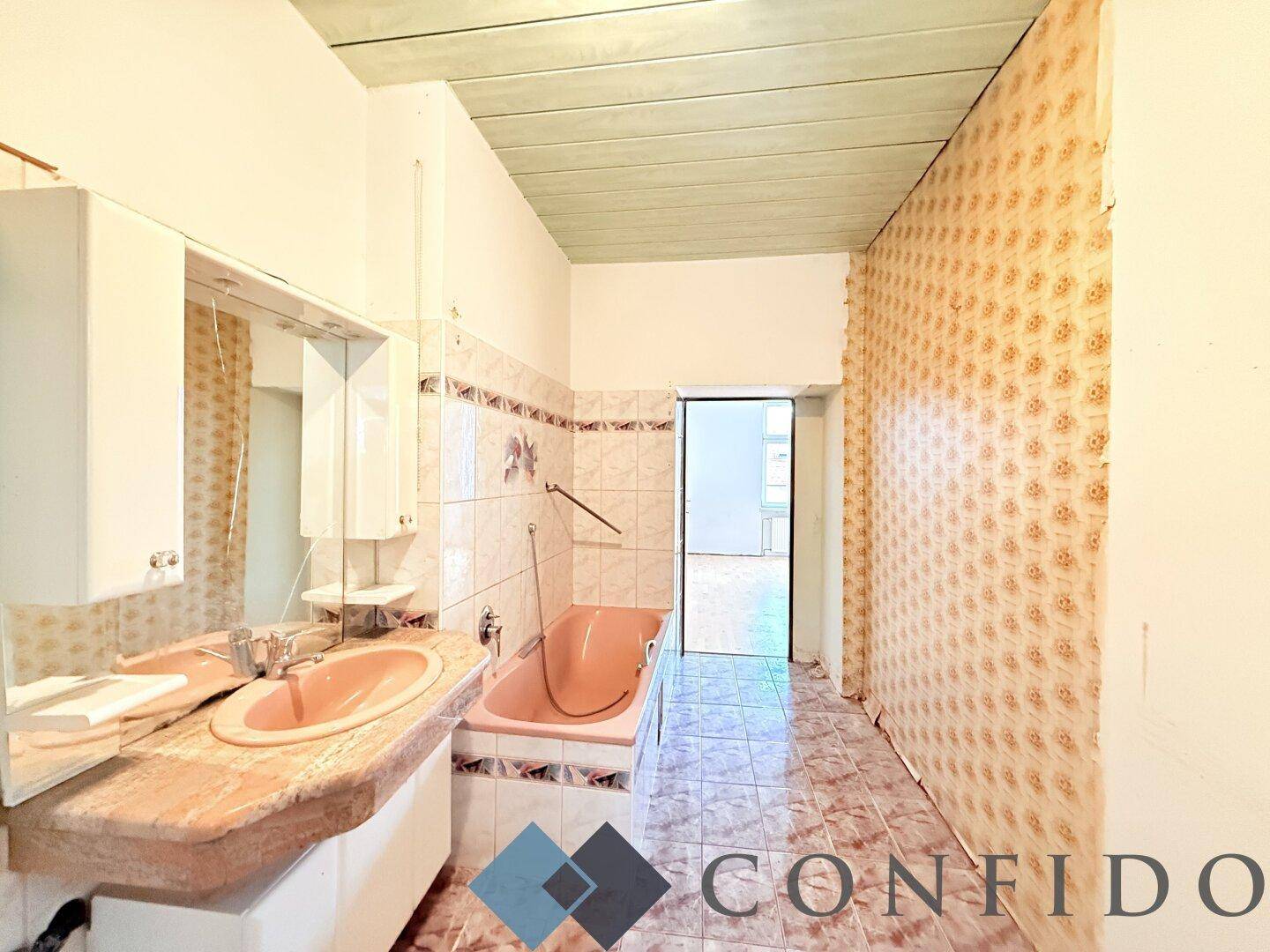 Badezimmer im 80er-Jahre-Stil mit rosa Badewanne, Waschbecken und gemusterten Fliesen.