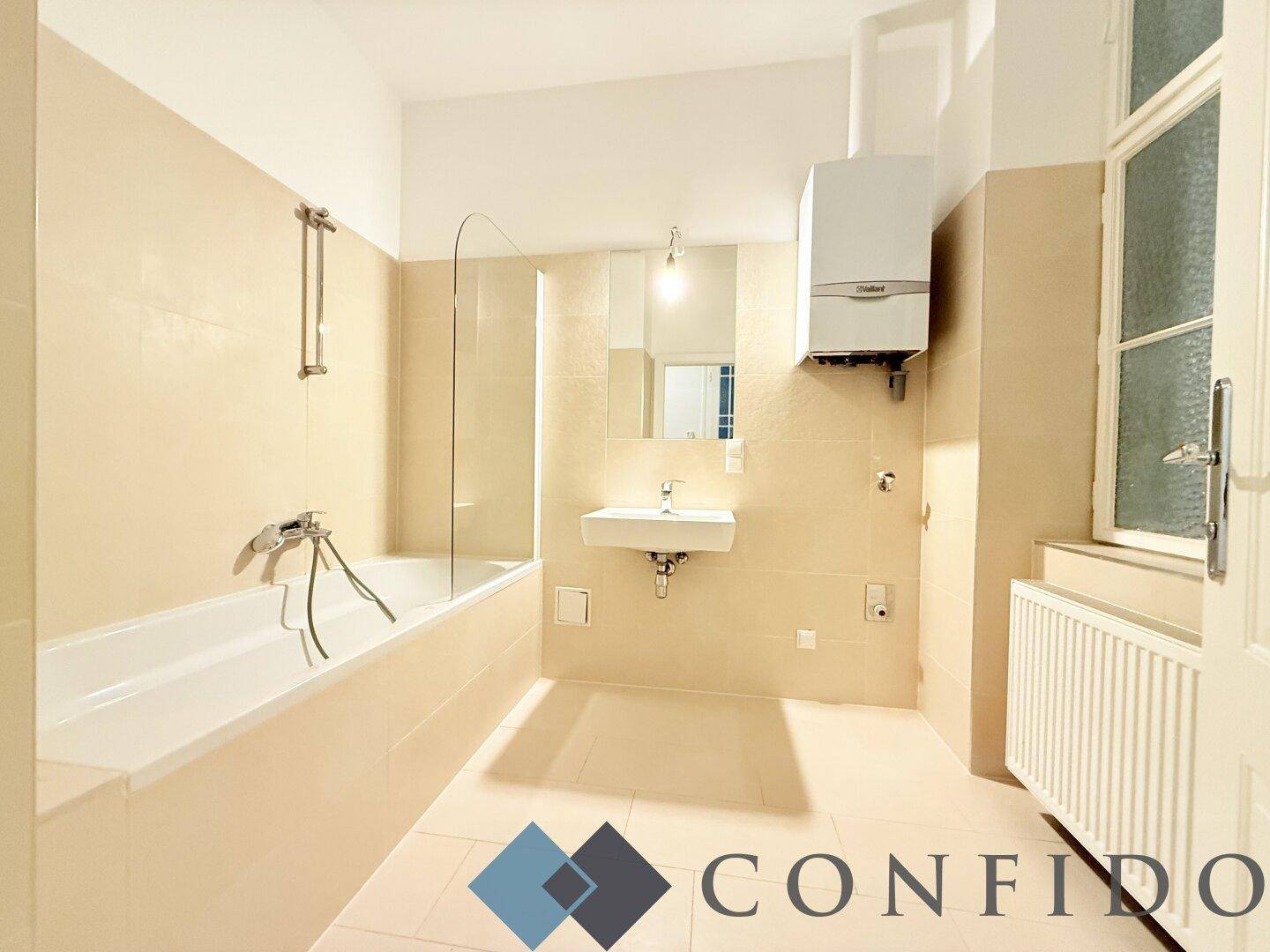 Helles Badezimmer mit Badewanne, Waschbecken und beigefarbenen Fliesen.