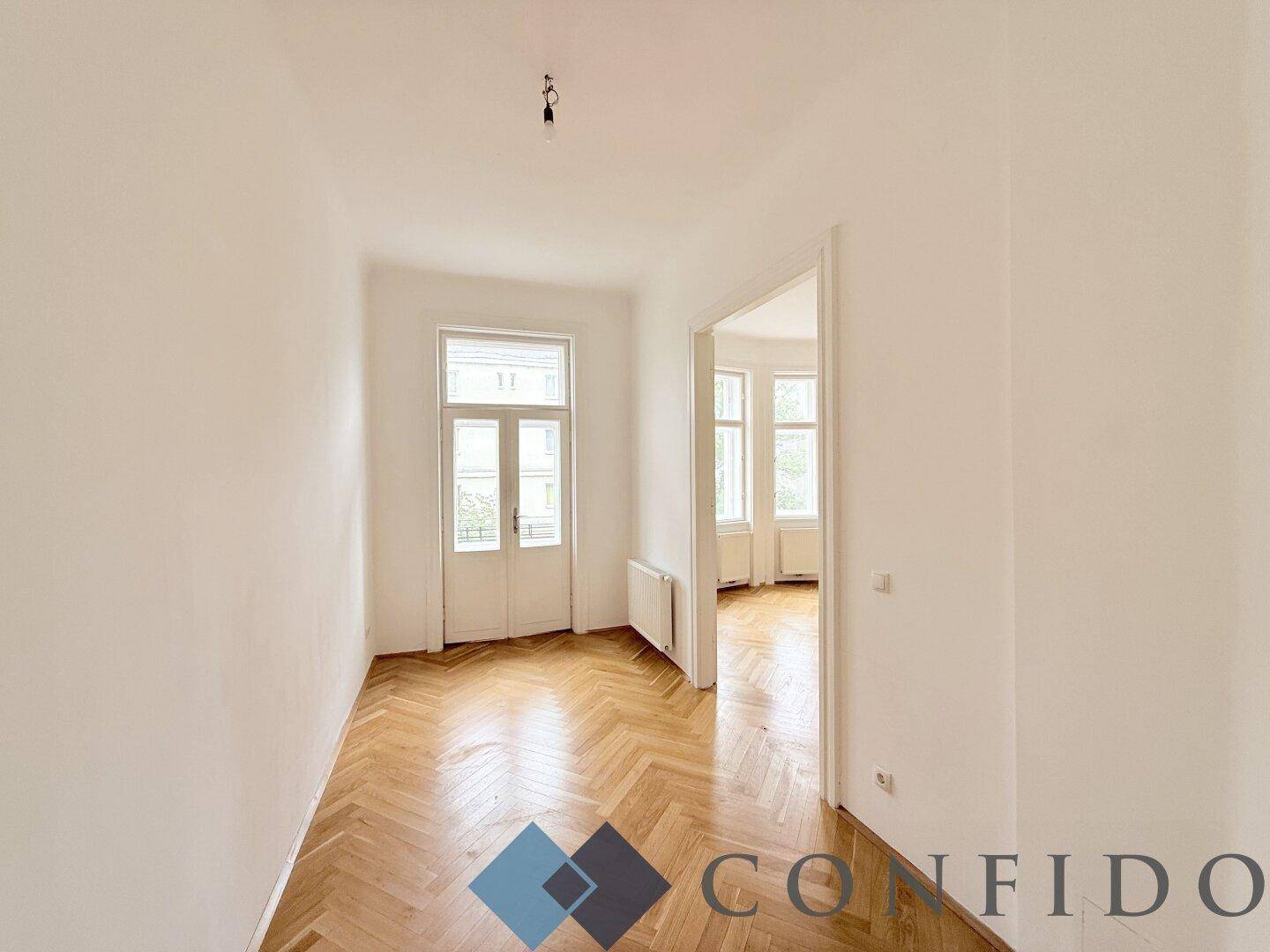 Heller Flur mit Fischgrätparkett und Zugang zu einem weiteren Zimmer.