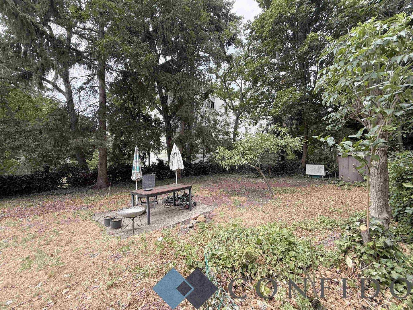 Großer Gartenbereich mit Rasenfläche, Bäumen und einem Sitzbereich im Freien.