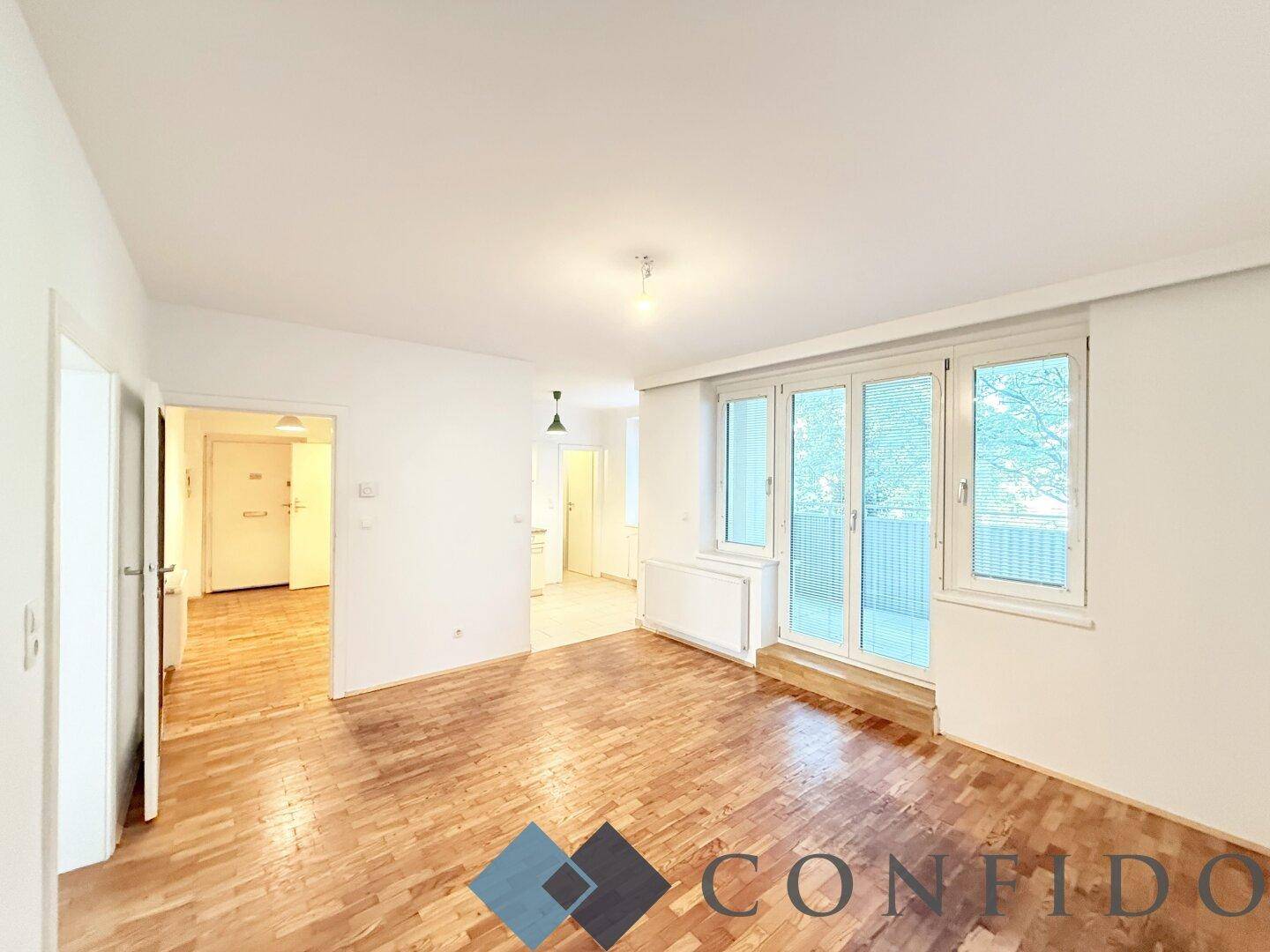 Geräumiges Wohnzimmer mit hellem Parkettboden und Zugang zum Balkon, bereit zur individuellen Gestaltung.