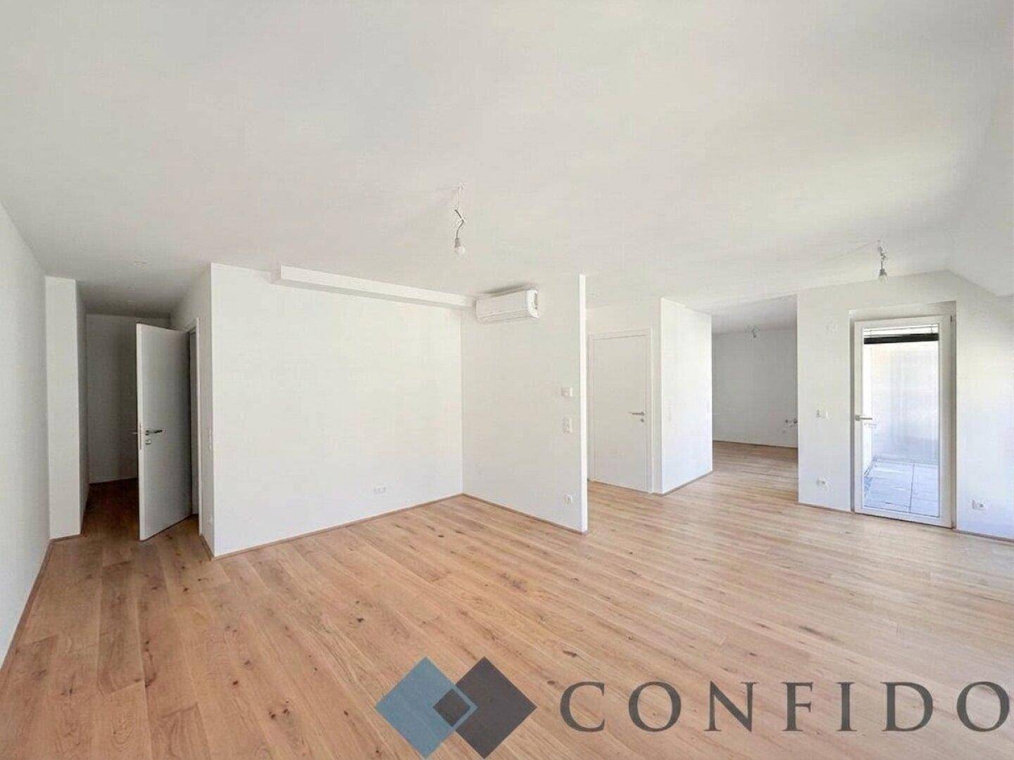 Geräumiger, heller Raum mit Holzboden und weiß gestrichenen Wänden, ideal für ein Wohnzimmer.