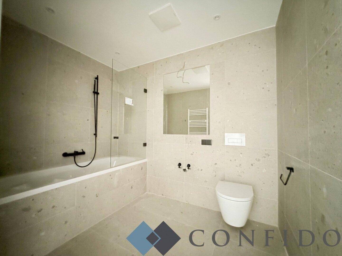 Modernes Badezimmer mit Badewanne, Wand-WC und hellen Fliesen an Wänden und Boden.