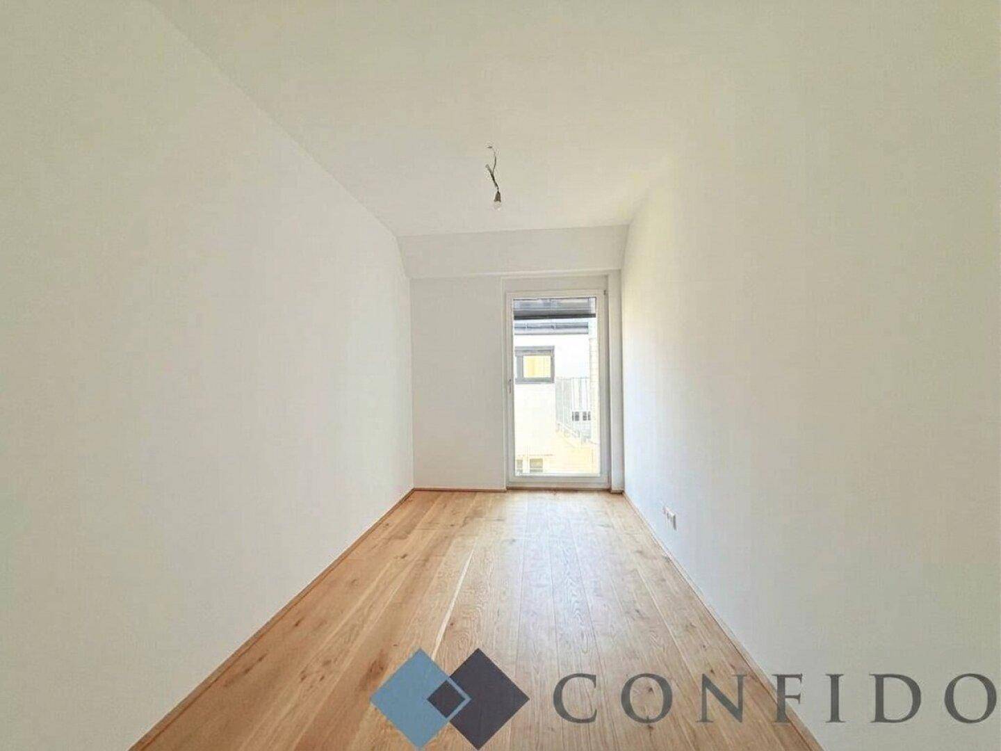 Helles Zimmer mit Holzboden und Zugang zu einem kleinen Balkon oder französischen Balkon.