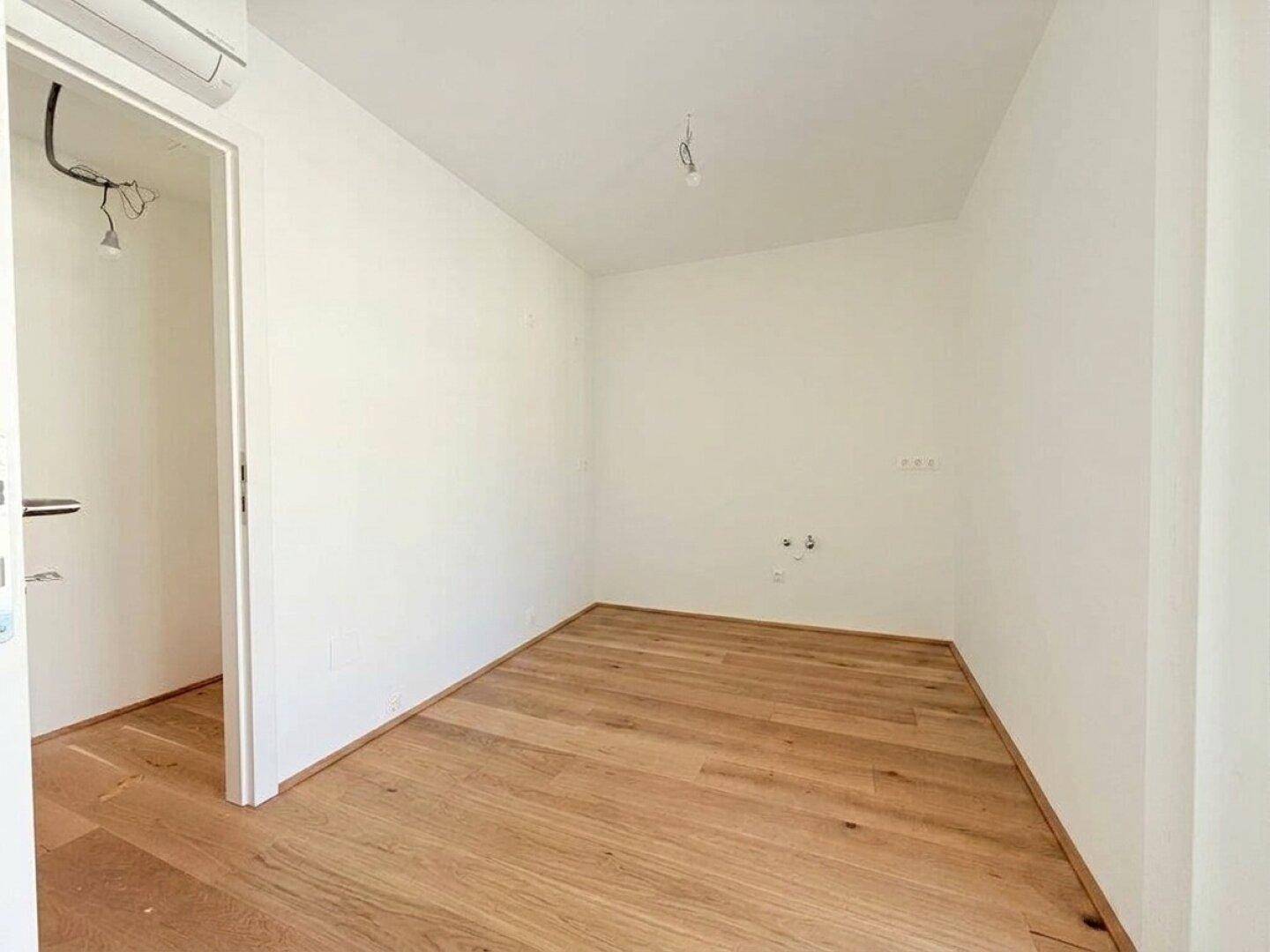Leeres Zimmer mit Holzboden und weiß gestrichenen Wänden, bereit zur individuellen Gestaltung.