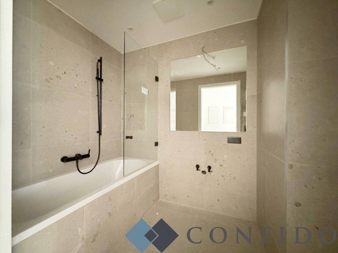 Modernes Badezimmer mit Badewanne, grauen Fliesen und minimalistischen Armaturen.
