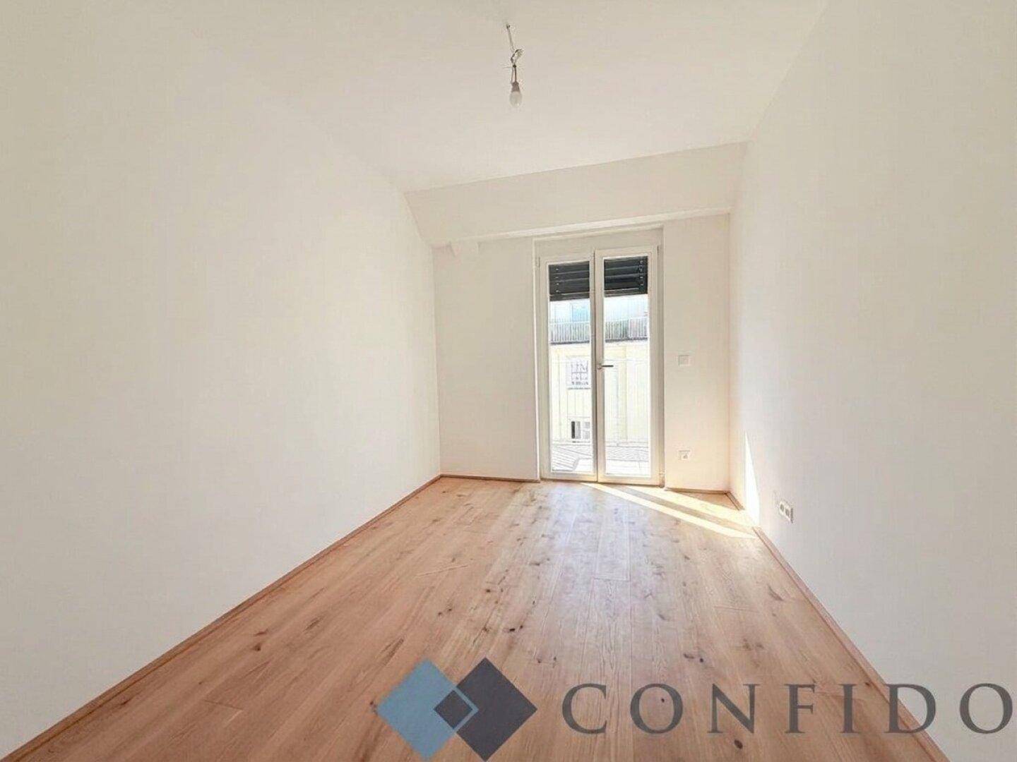 Helles Schlafzimmer mit Holzboden und Fenster, das viel natürliches Licht hereinlässt.