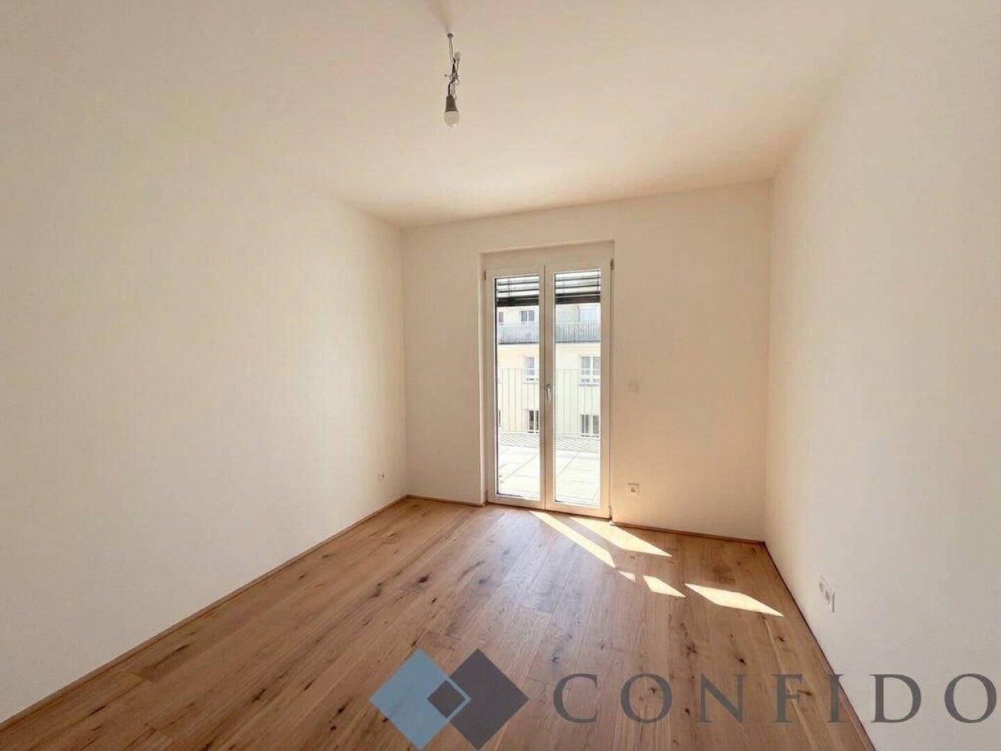 Helles Schlafzimmer mit Parkettboden und großem Fenster, bereit für individuelle Gestaltung.