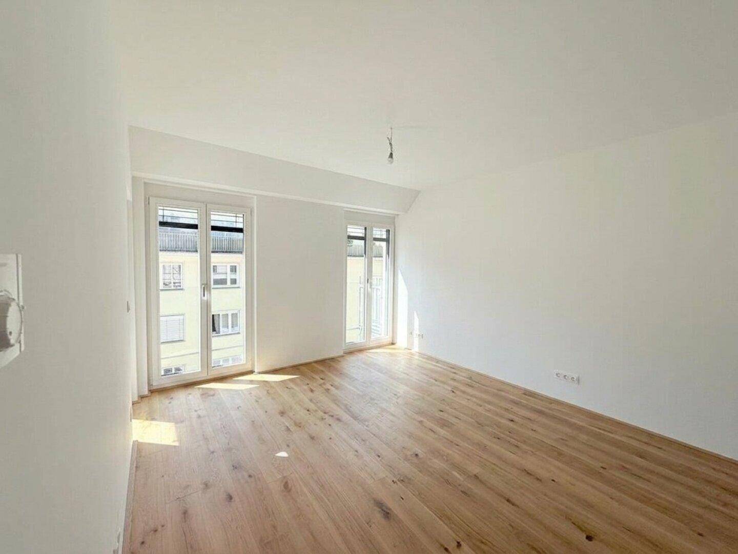 Lichtdurchfluteter Raum mit Holzboden und Zugang zu einem französischen Balkon, ideal für ein Schlafzimmer.