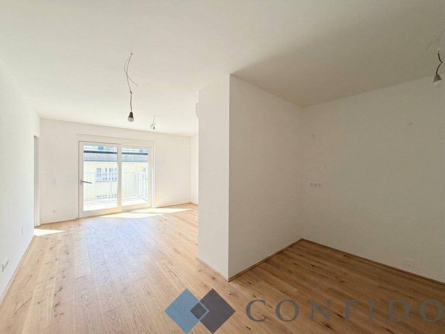 Heller, leerer Wohnbereich mit Holzboden und Zugang zu einem Balkon.