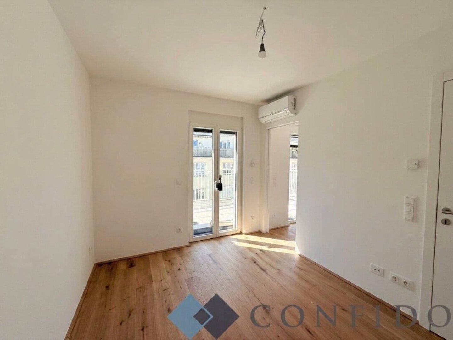 Helles Schlafzimmer mit Holzboden, Klimaanlage und Zugang zum Balkon.
