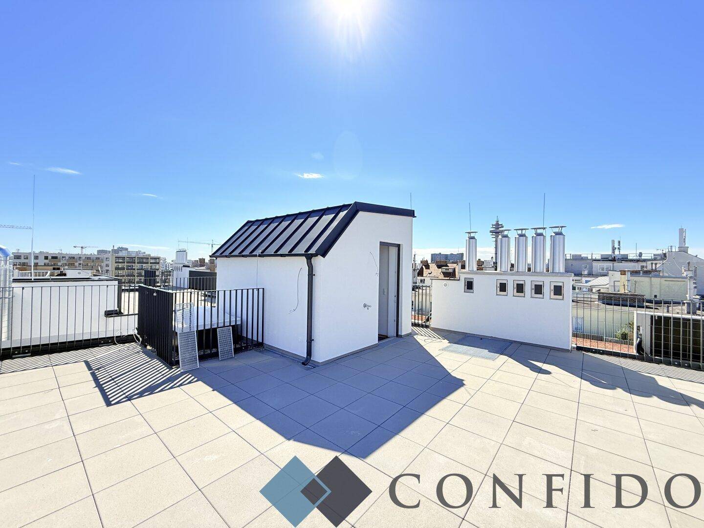 Sonnige Dachterrasse mit moderner Gestaltung und weitem Stadtblick unter klarem Himmel.