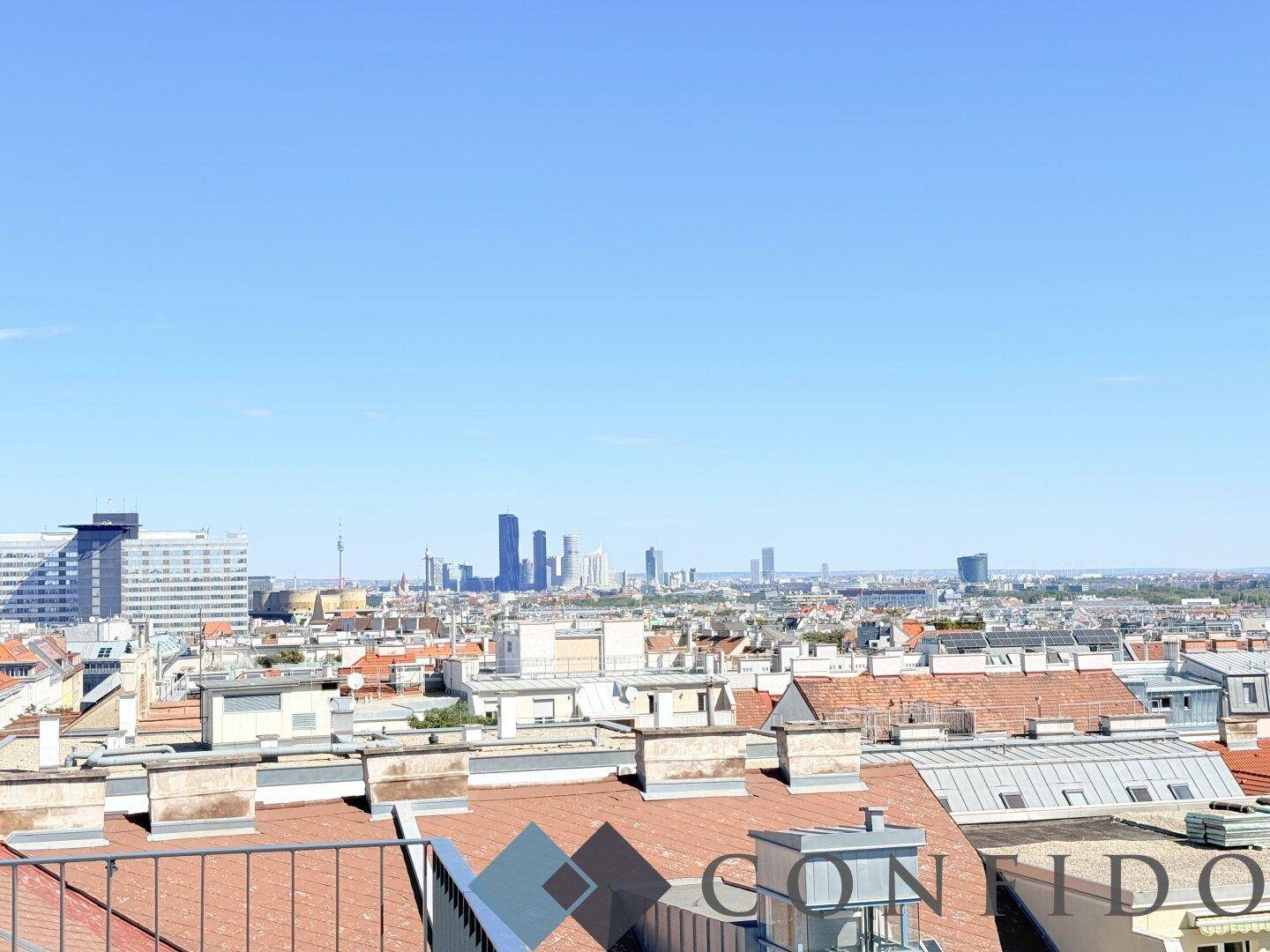 Panoramablick über die Dächer der Stadt mit moderner Skyline im Hintergrund und blauem Himmel.