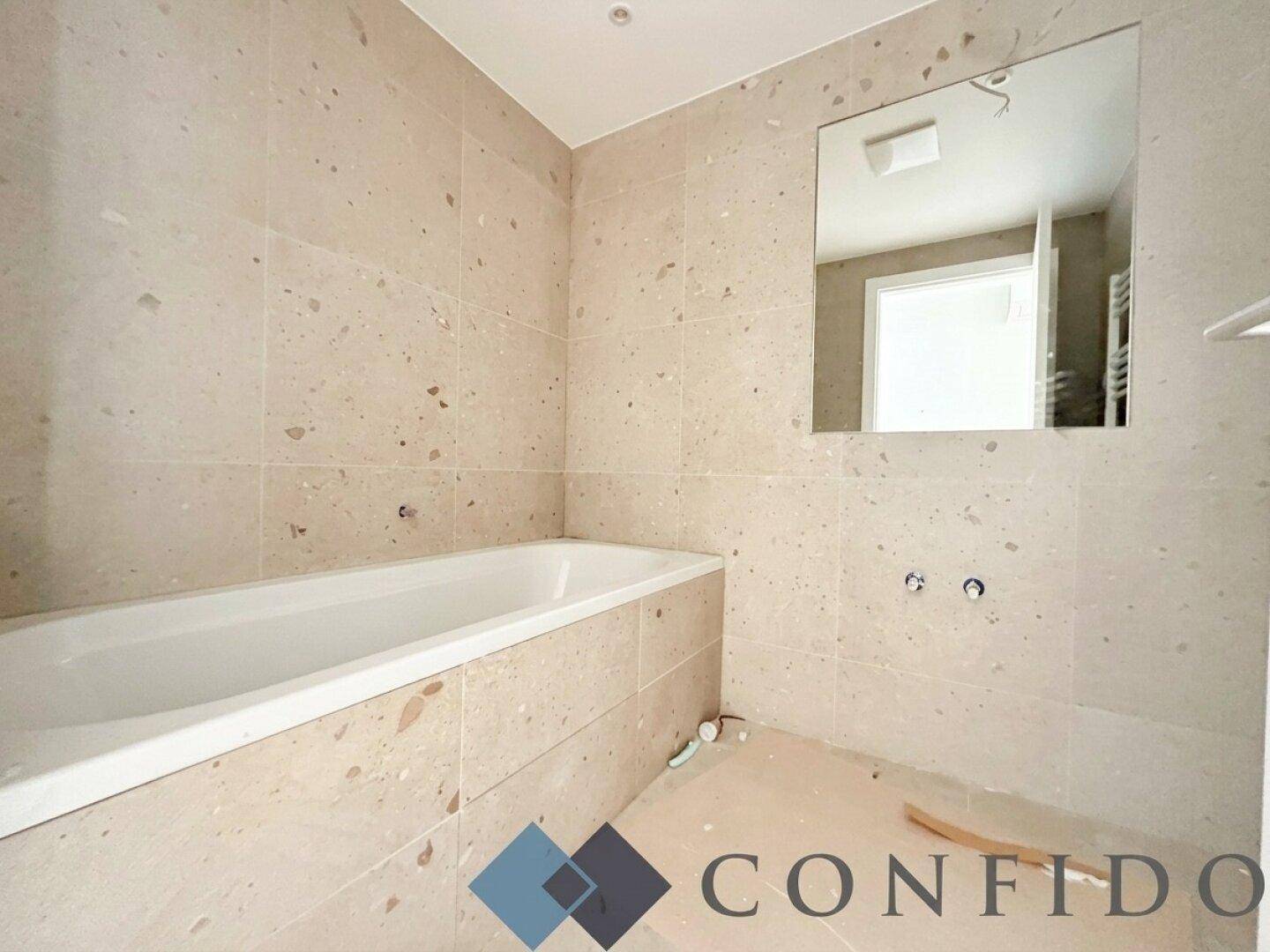 Modernes Badezimmer in Bau mit Badewanne und beigefarbenen Fliesen an Wänden und Boden.