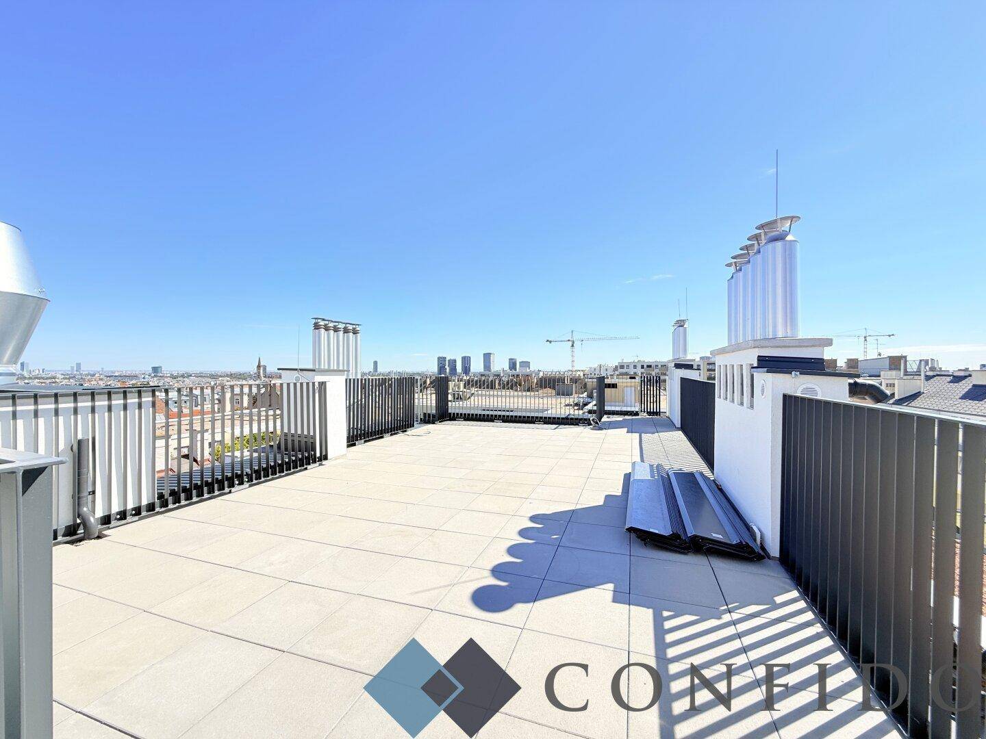 Große Dachterrasse mit weitem Blick über die Stadt und moderne Architektur im Hintergrund.